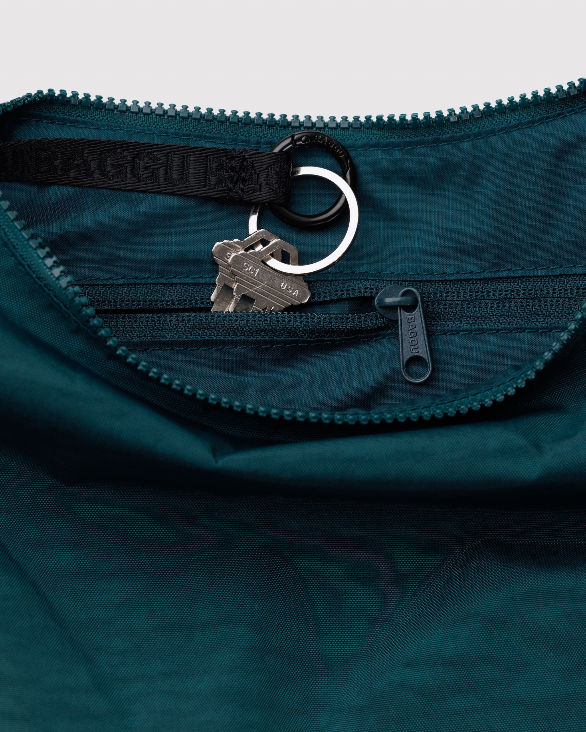 Close-up of a teal bag with a zipper and keychain detail.