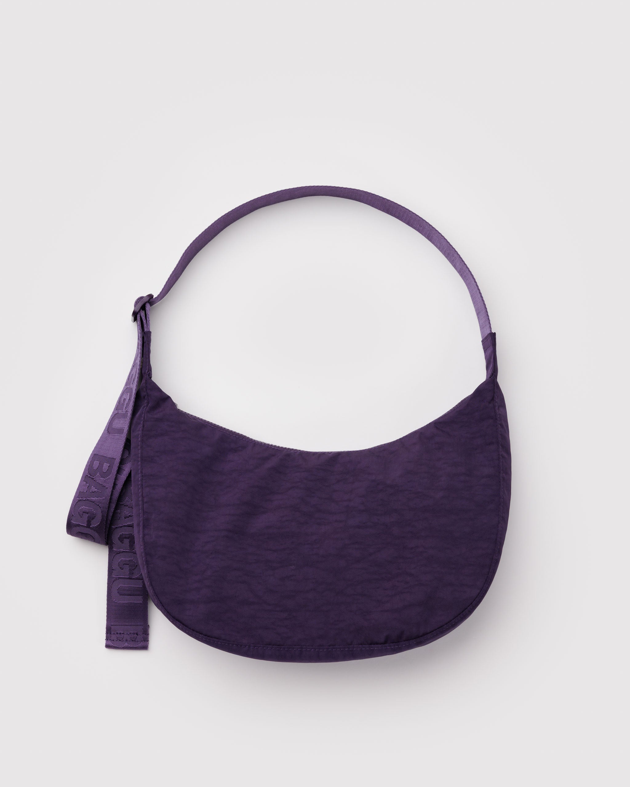 Purple shoulder bag in a crescent shape with a long wide webbed adjustable strap and top zip.