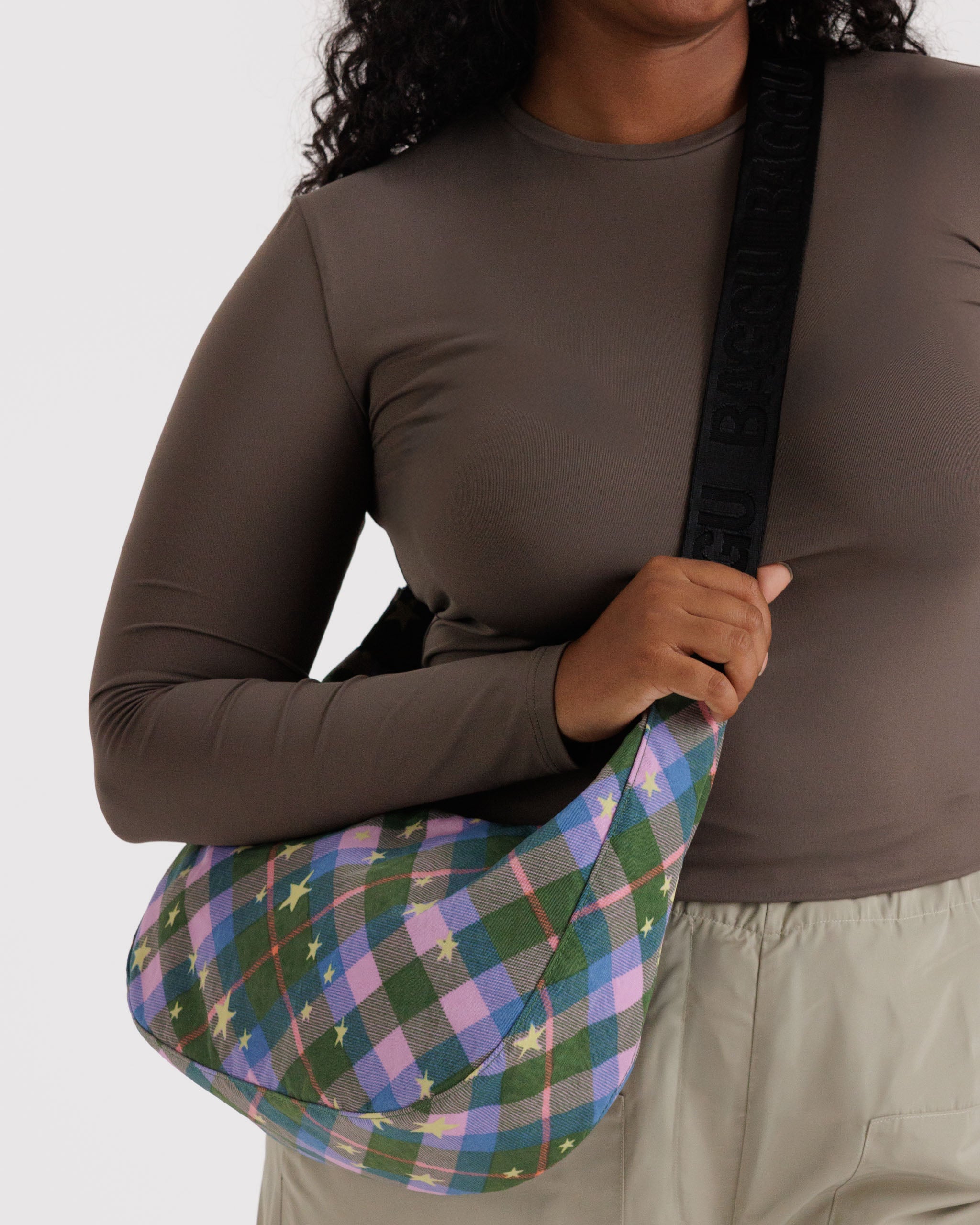 Person holding black strap of a green and pink plaid bag.