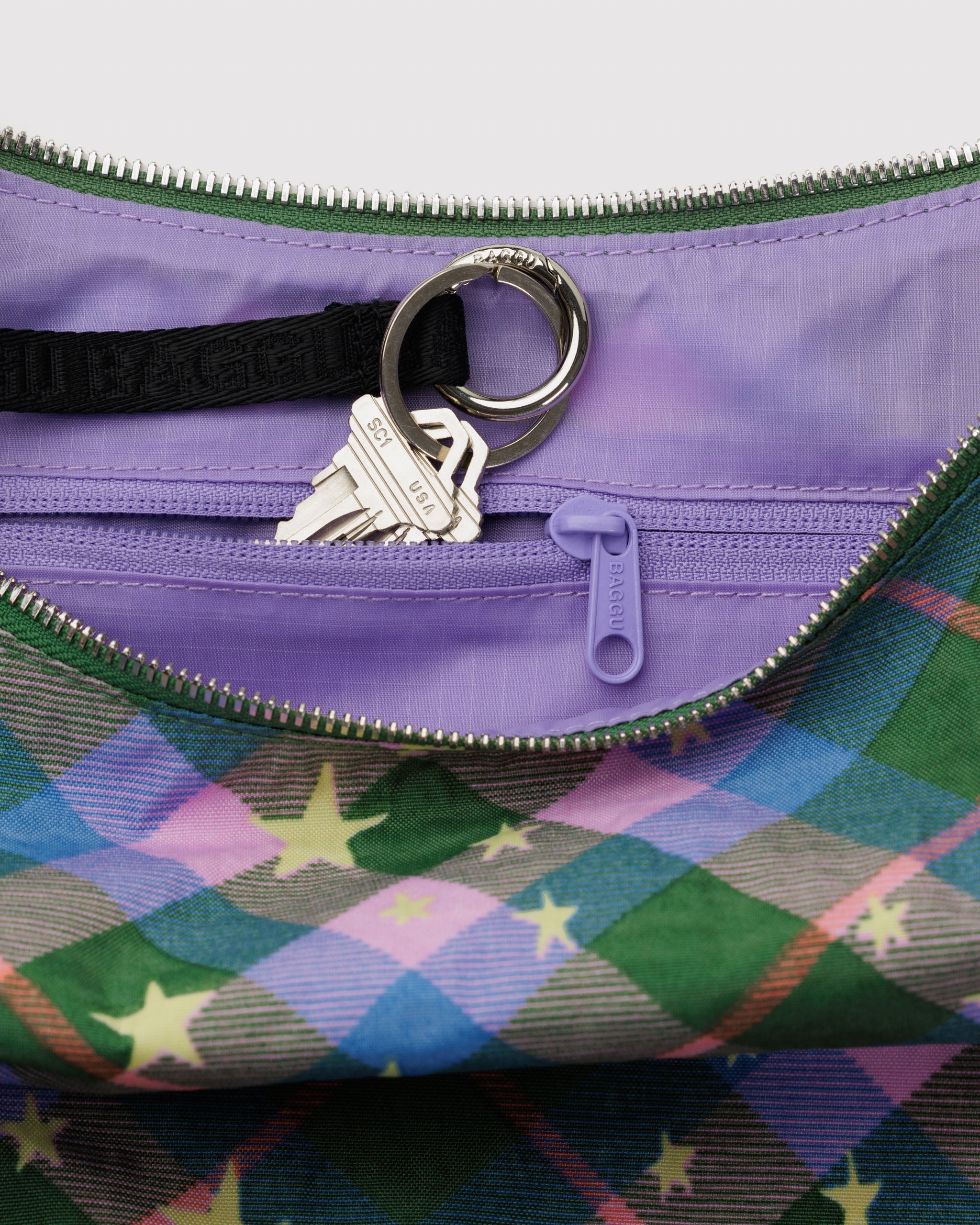 Colourful green plaid patterned bag and stars print with purple lining inside, a zippered pouch and keys on a black keyleash.