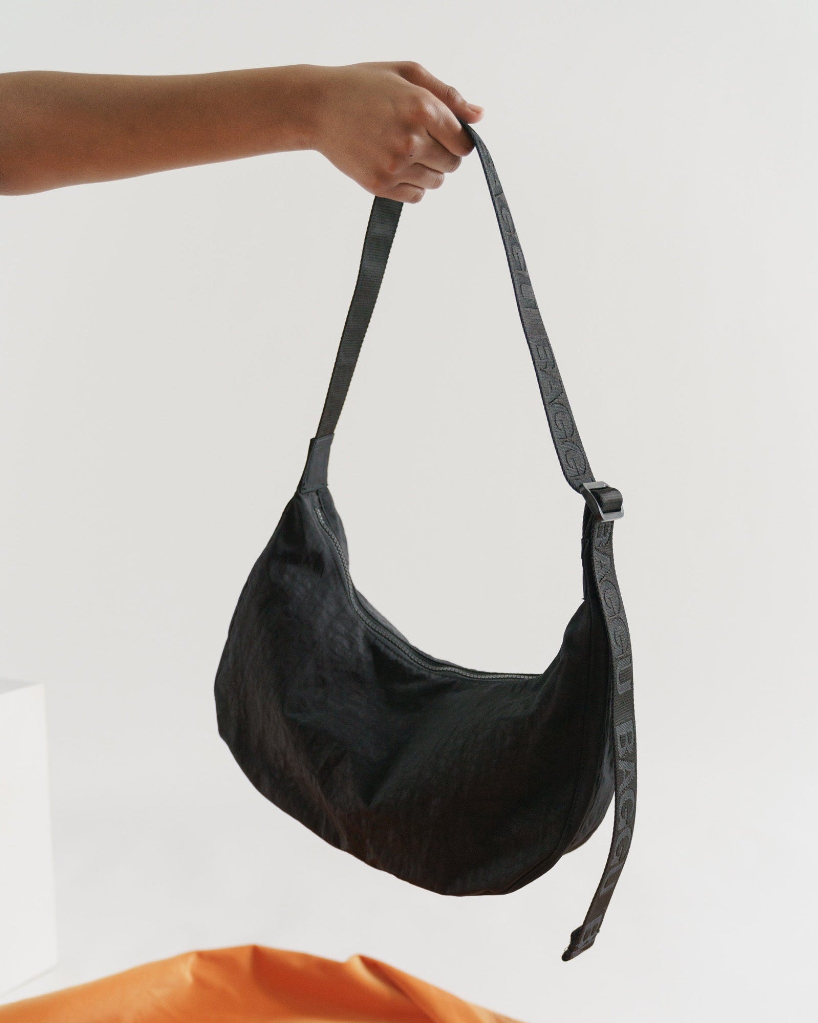 Black shoulder bag held by a person by the adjustable shoulder strap with a zip top