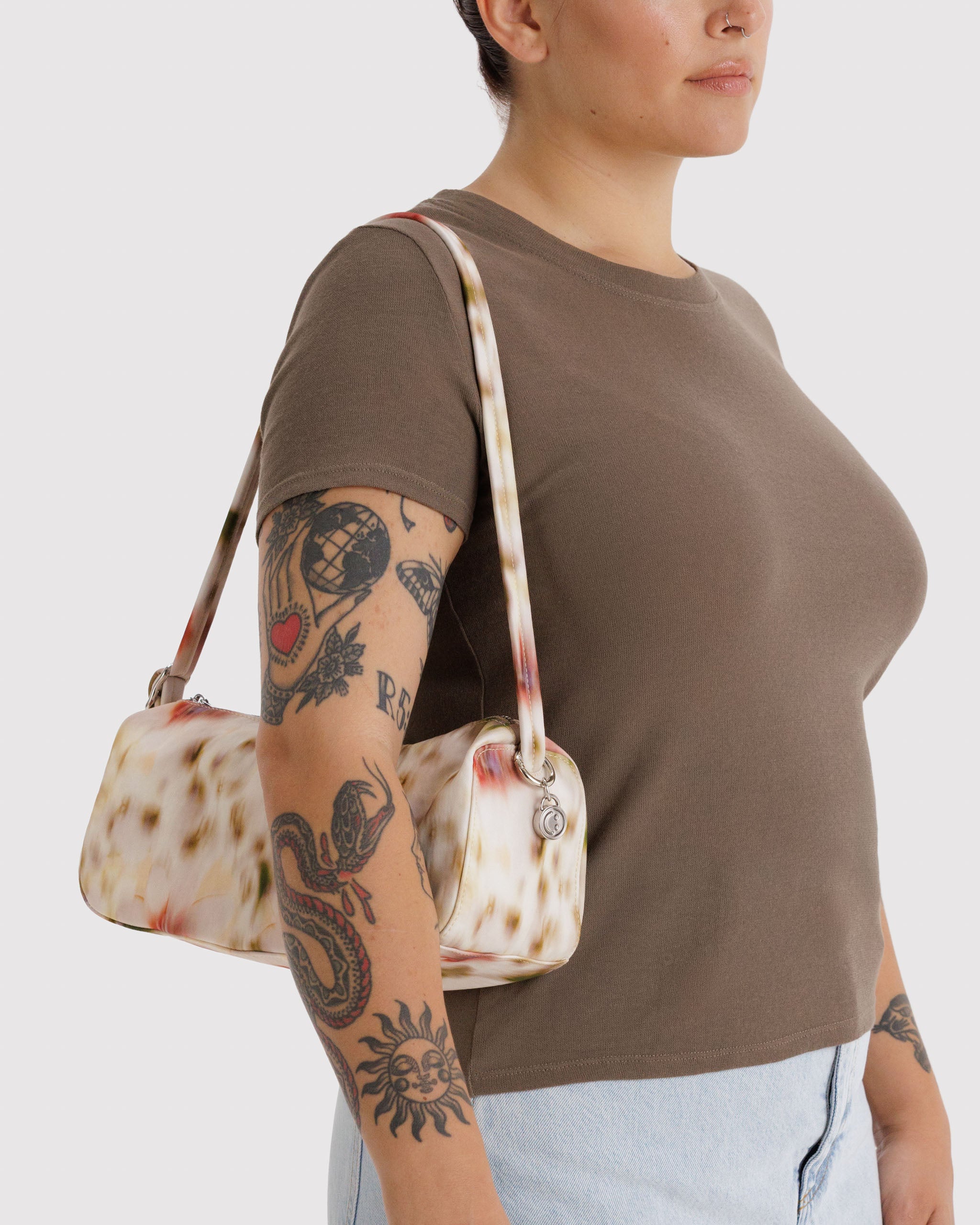 Person wearing a brown shirt and light blue jeans, holding a cream patterned handbag on shoulder.