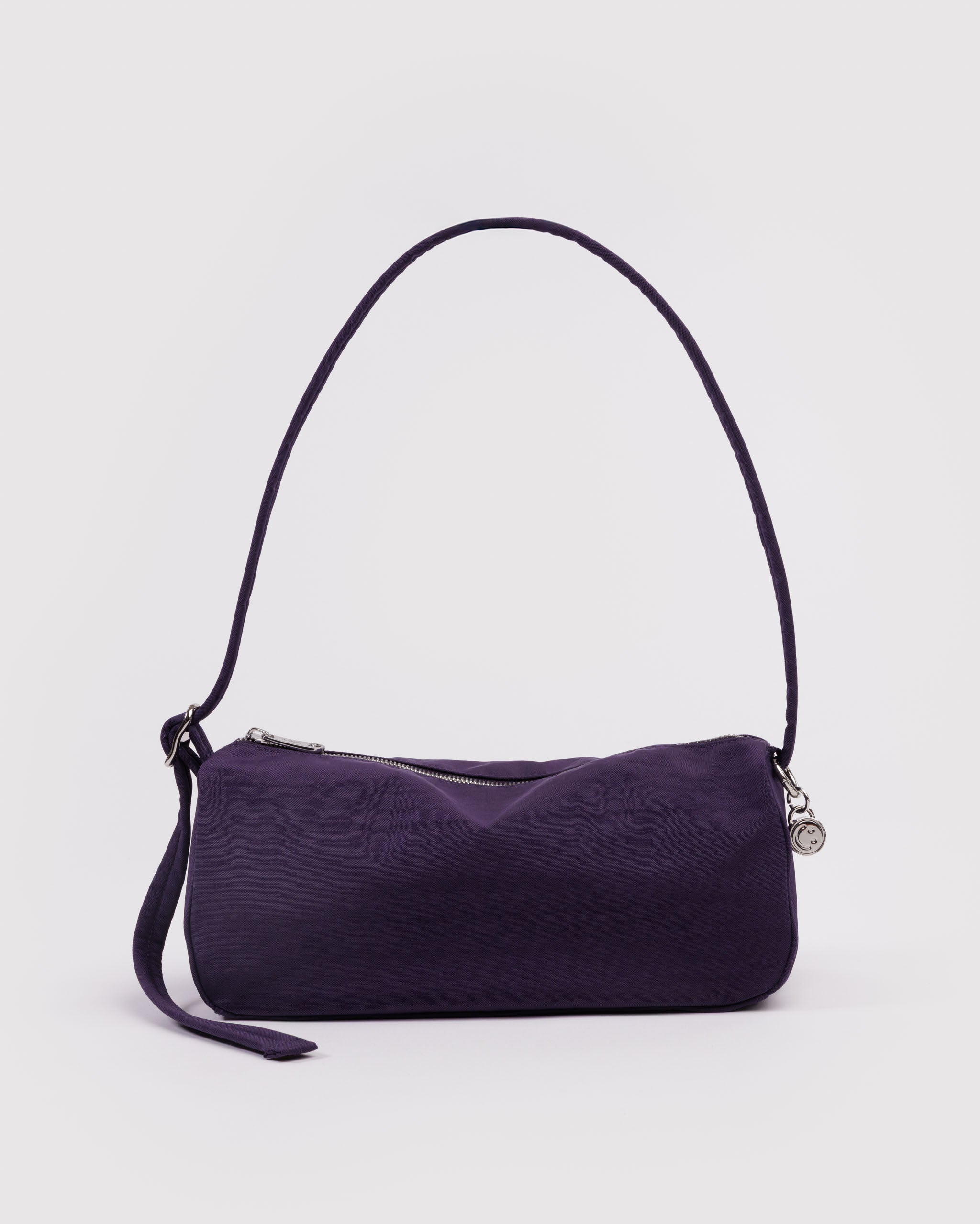 Purple handbag with an adjustable shoulder strap and silver metal hardware, zip and smiley face bag charm.