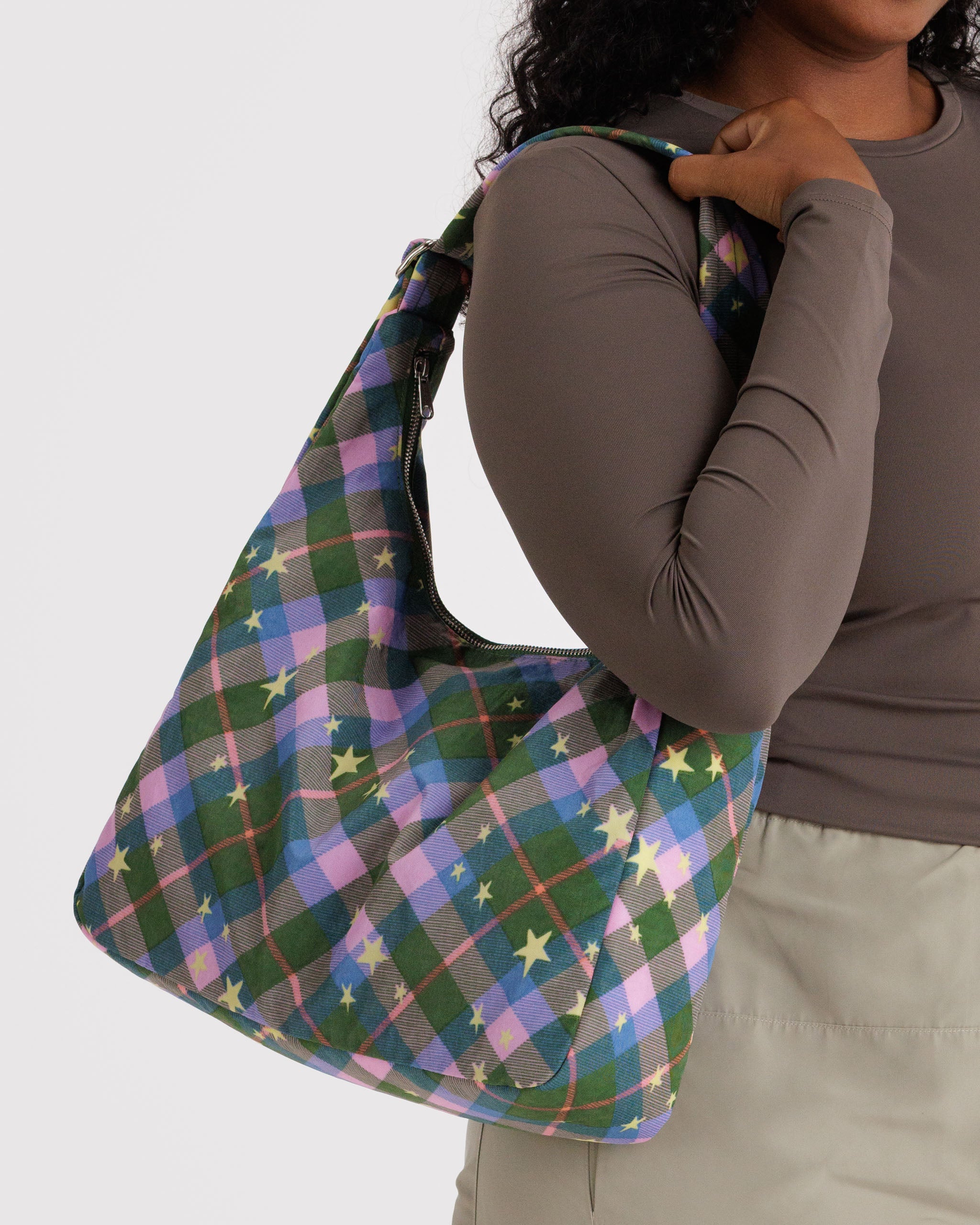 Person holding a green plaid bag with star patterns on shoulder with zip top and adjustable strap.