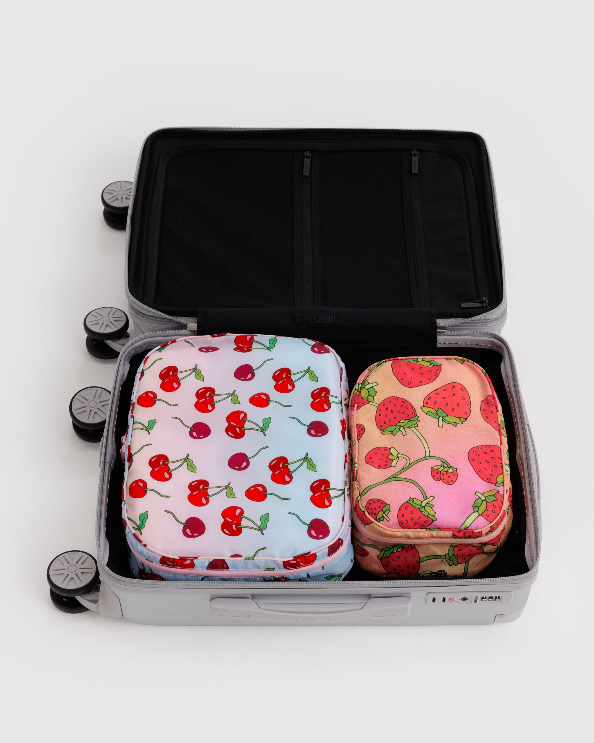Set of two fabric packing cubes in a medium and small size with cherry and strawberry pattern packed inside an open suitcase.