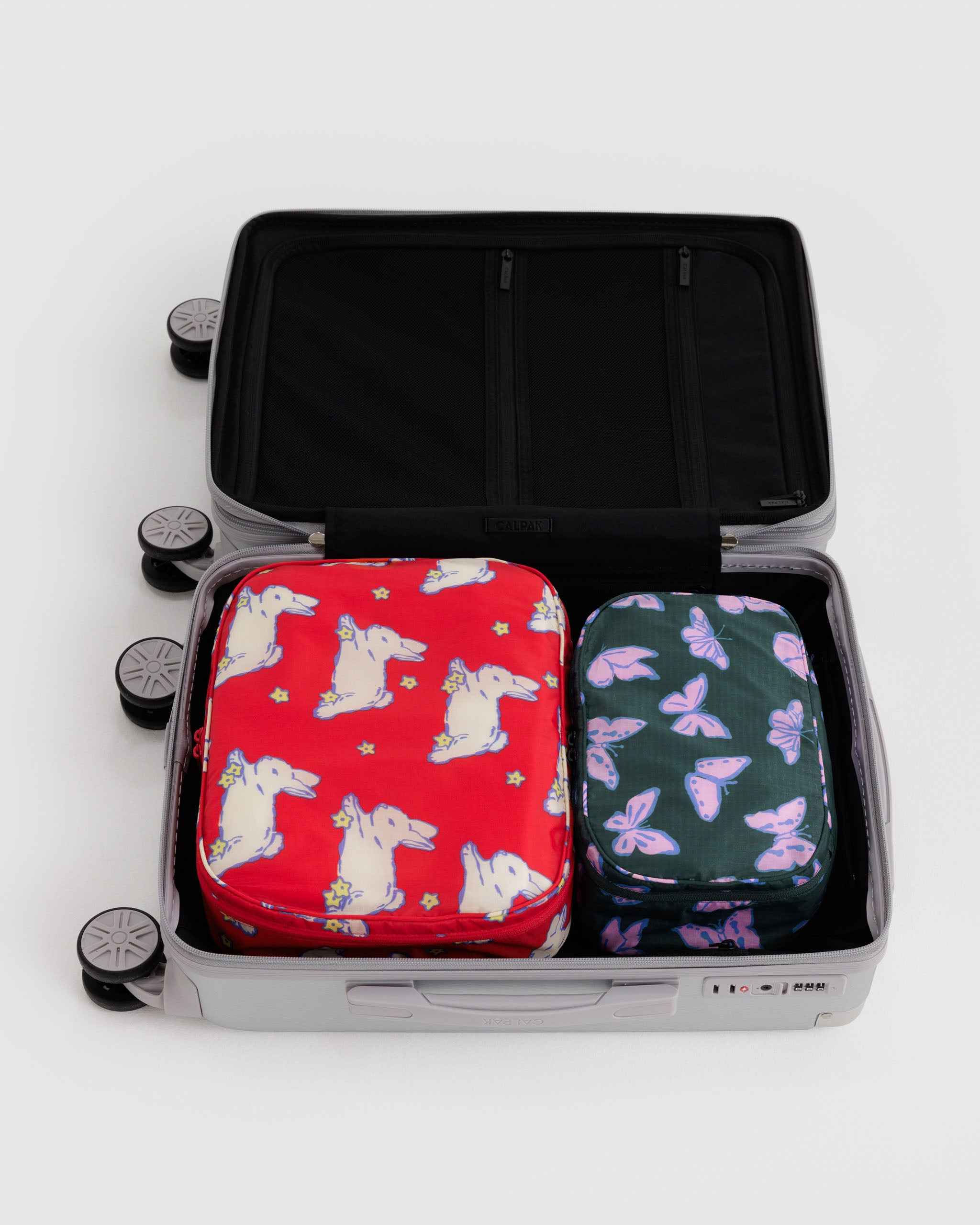 Two patterned bags, a medium size red with bunny design and a small green with butterfly design, inside an open suitcase.