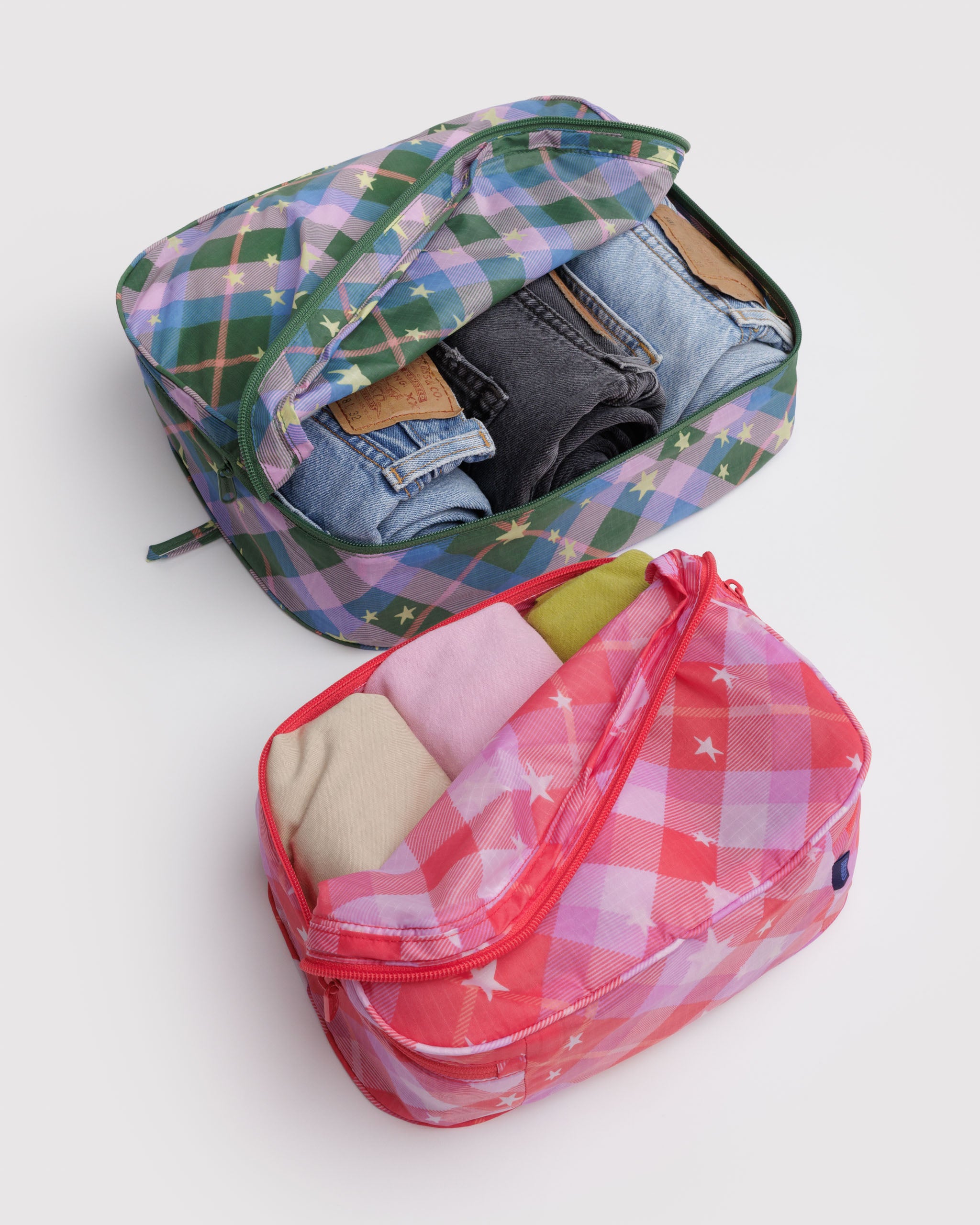 Two different sized plaid and stars patterned packing cubes, zip open and folded back with clothes inside.