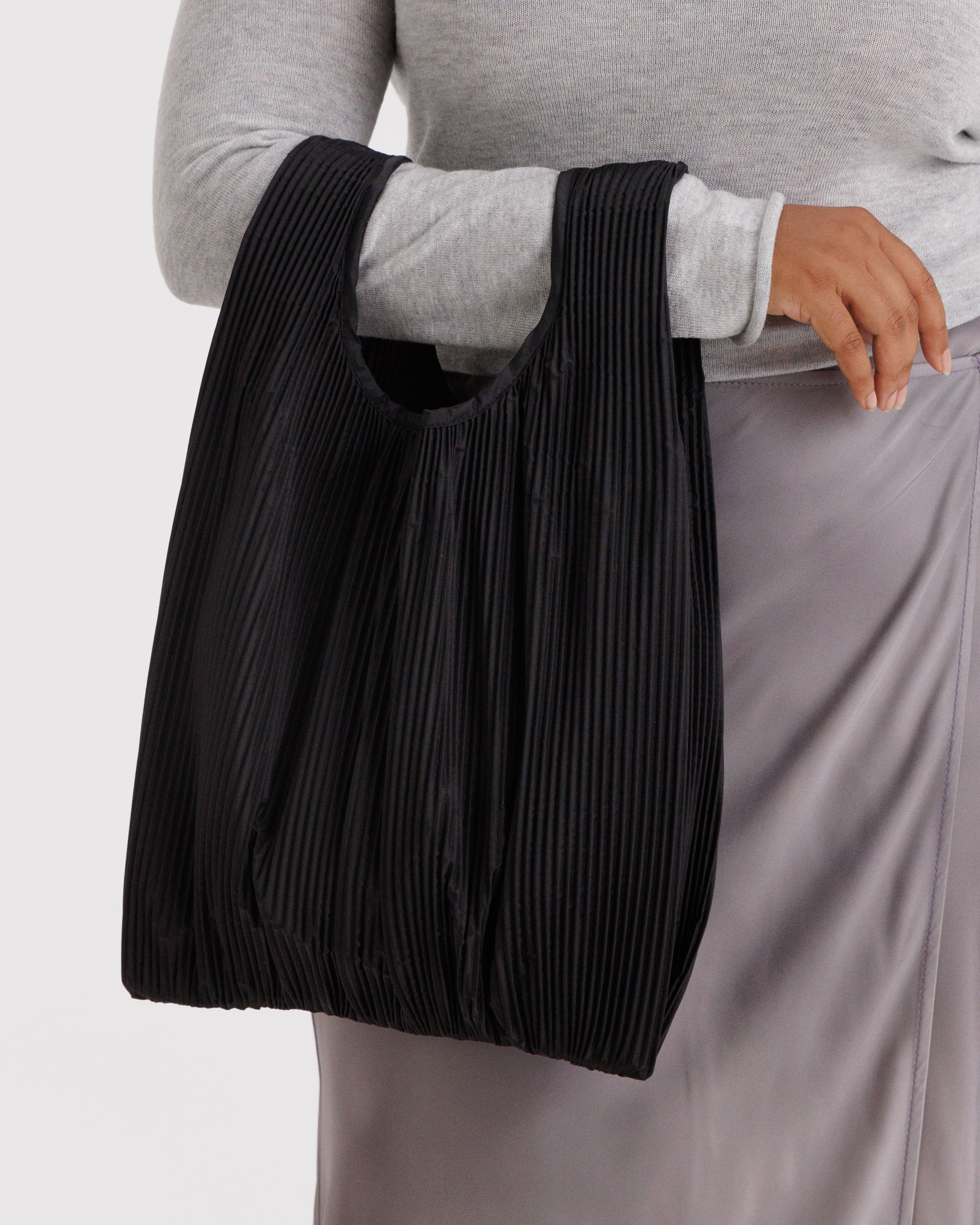 Person holding a black pleated tote bag on arm.