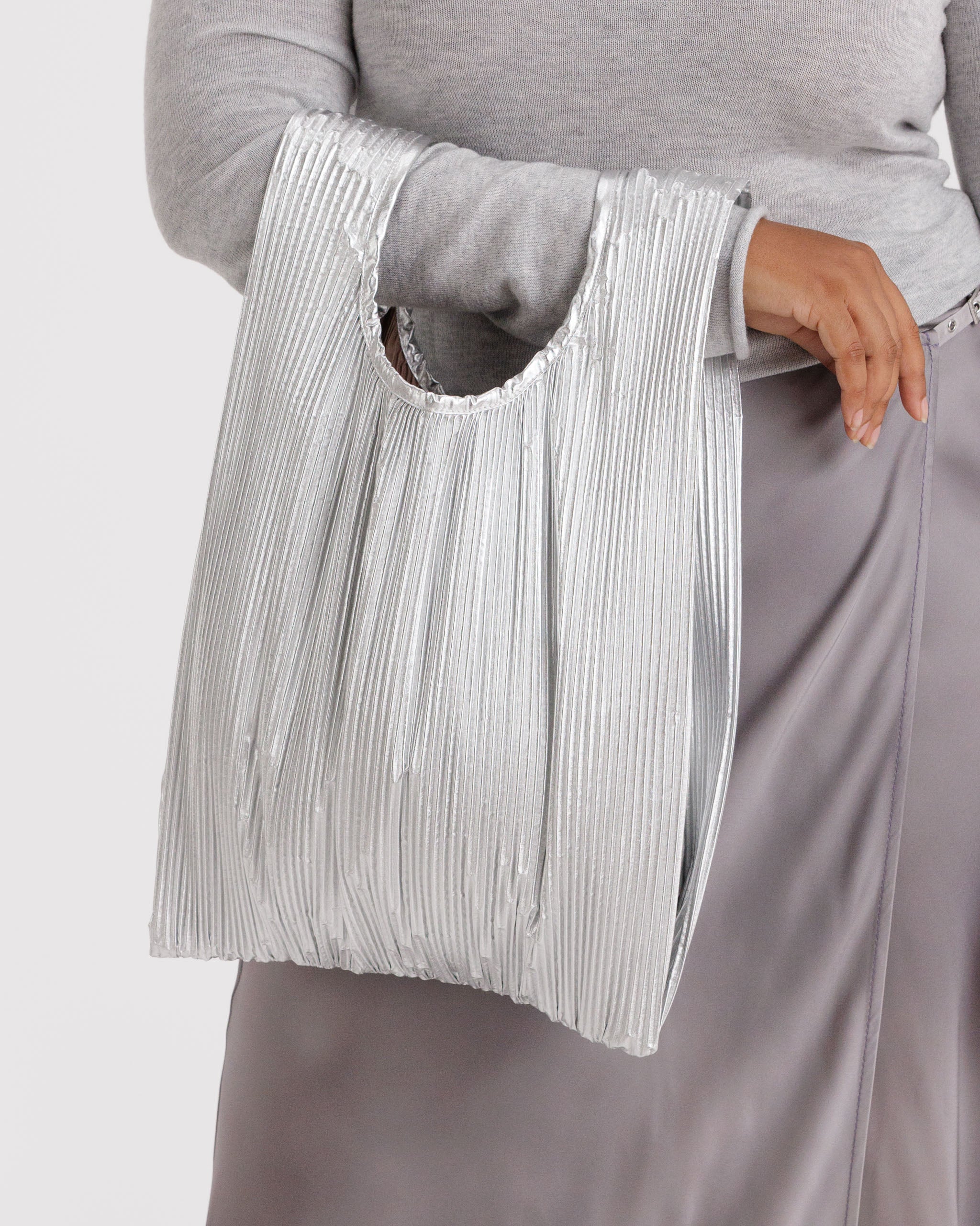 Person holding a mini pleated shiny chrome metallic bag.