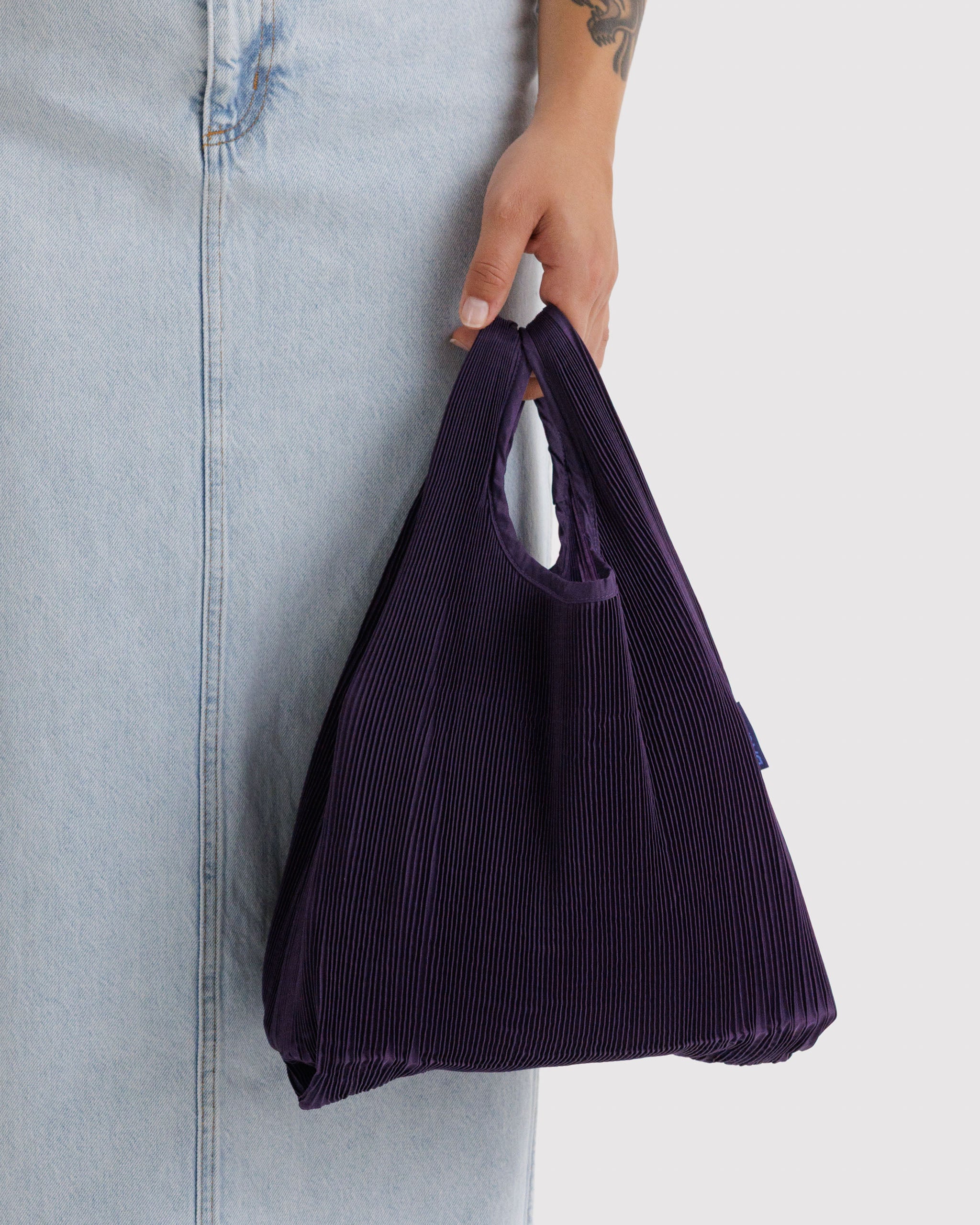 Person holding a purple pleated tote bag in their hand.