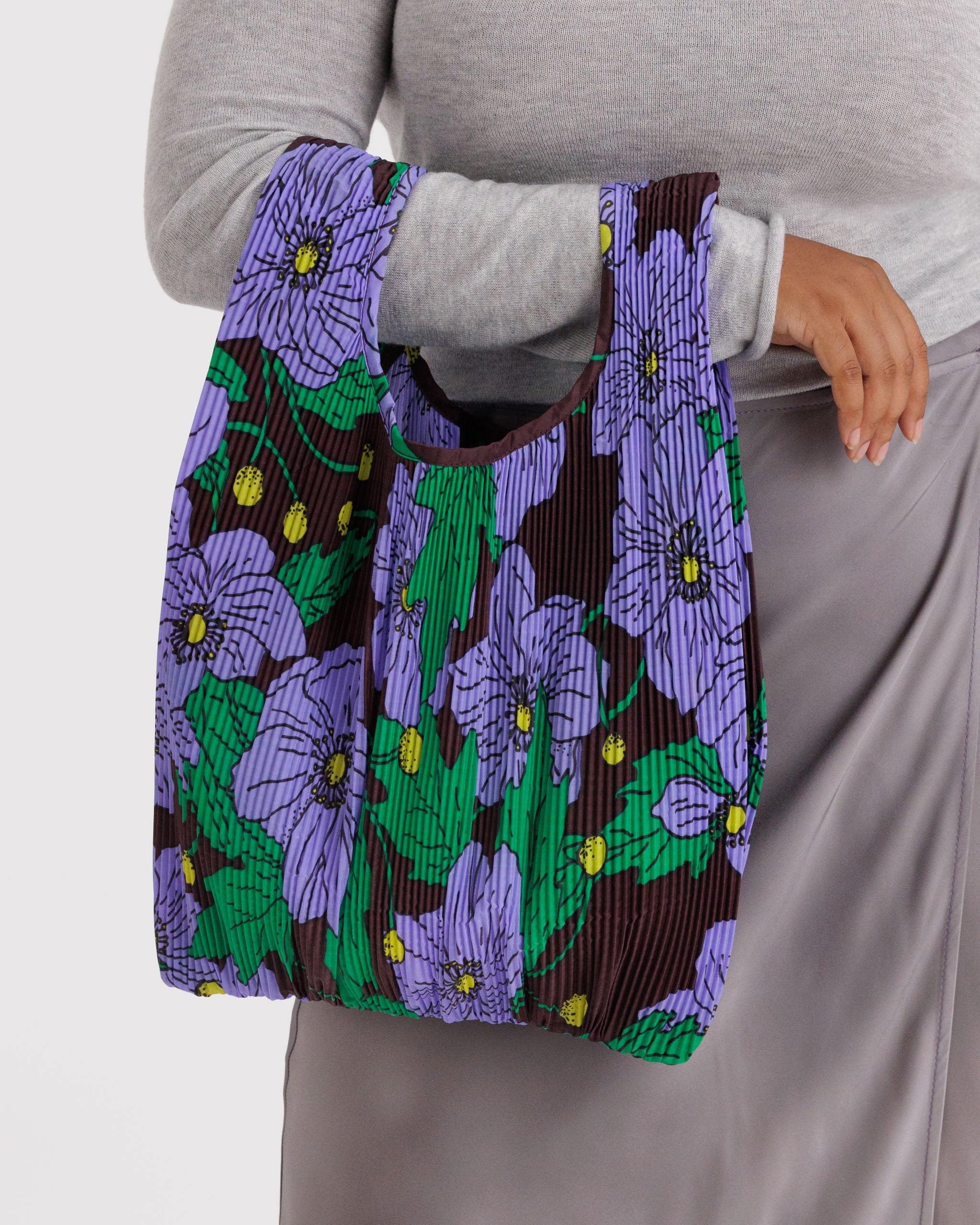 Person holding a maroon pleated reusable tote bag with purple poppy floral pattern.