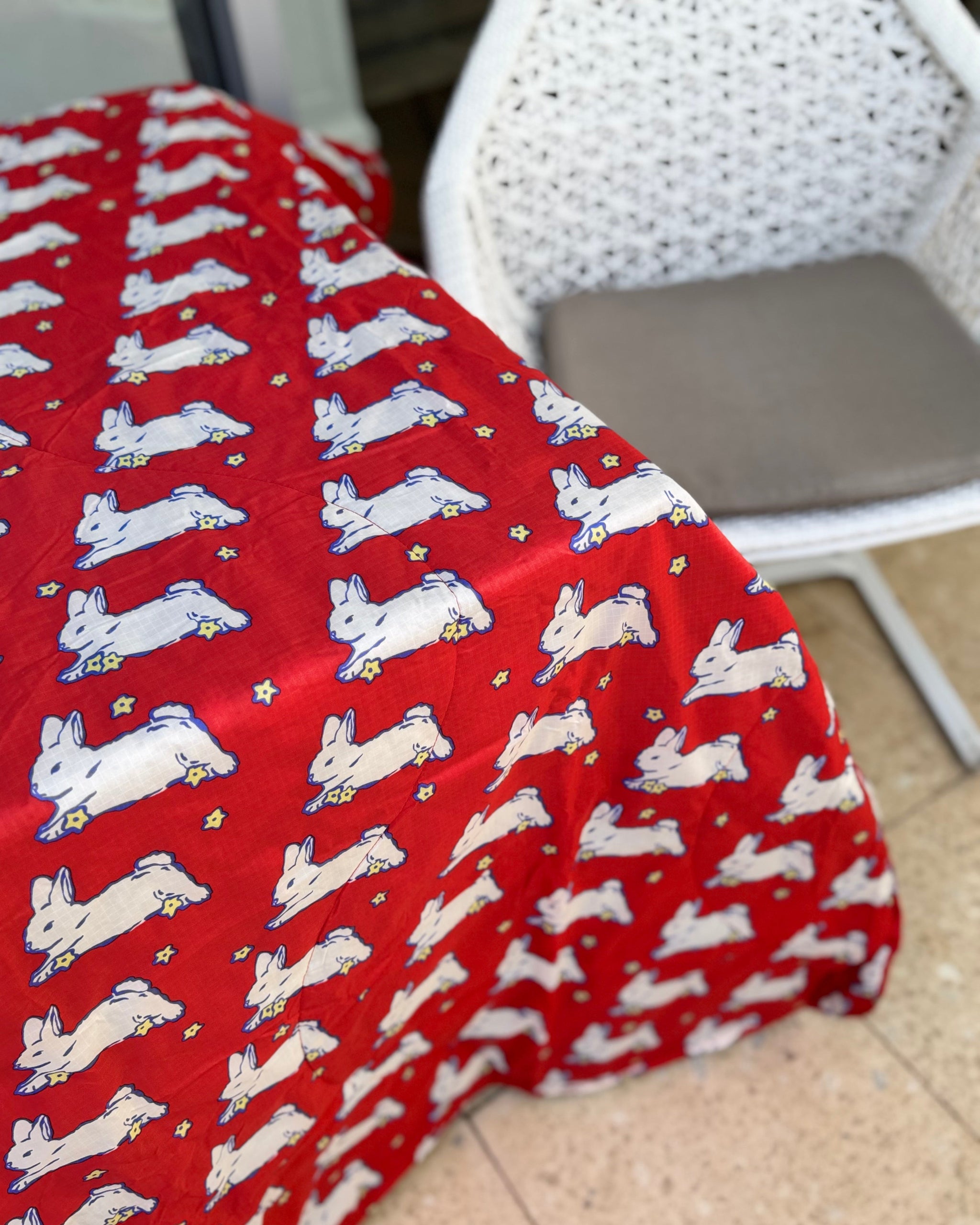 Red quilted picnic blanket with white bunnies and small yellow flowers pattern laid on a table.