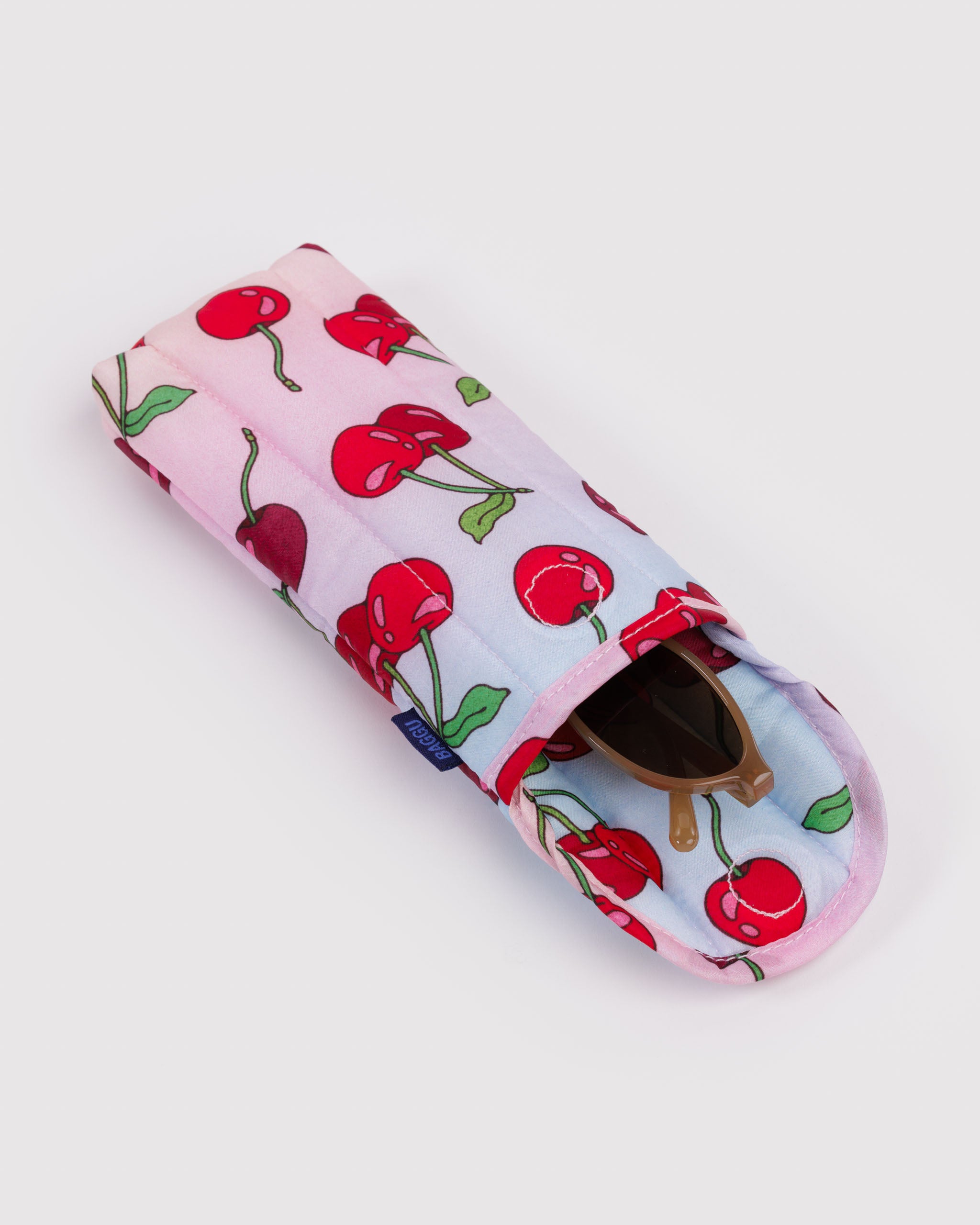 Puffy and quilted eyeglasses sleeve with cherry pattern on a light pink and blue background with sunglasses inside.