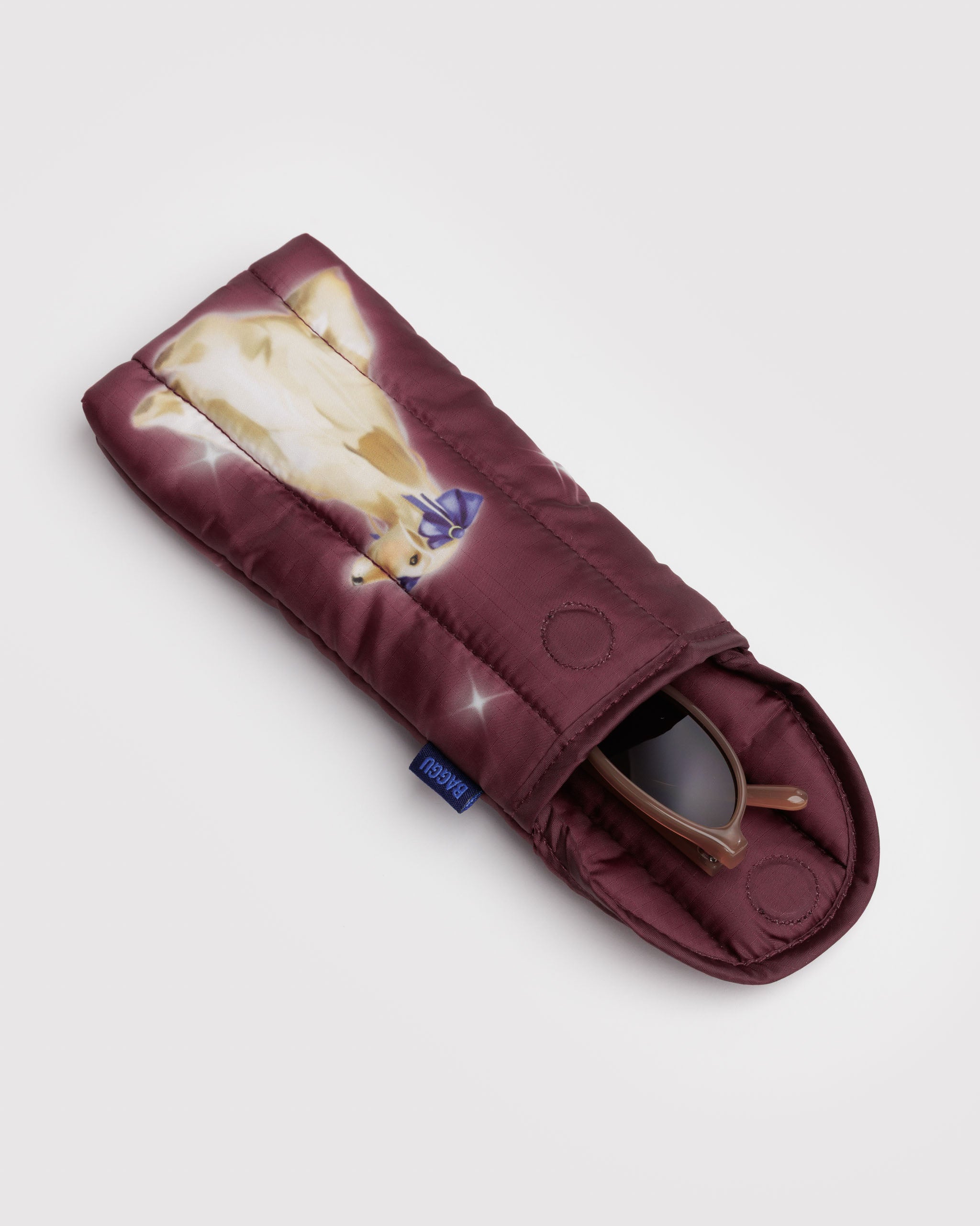 Quilted maroon glasses sleeve with a dog design, blue baggu label at side and magnetic closure top with glasses inside.