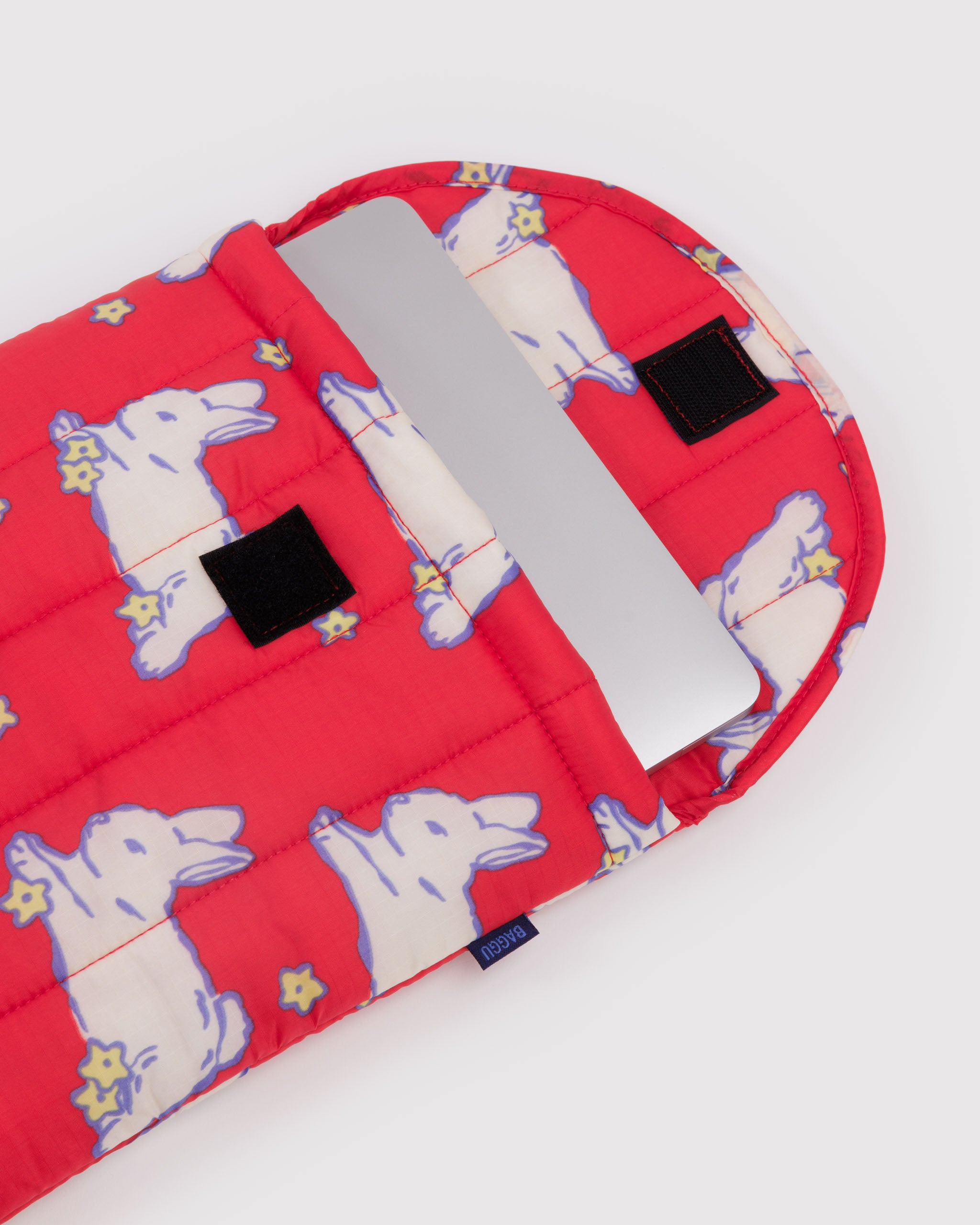 Top open on red quilted laptop sleeve with rabbit pattern and velcro closure with silver laptop inside.