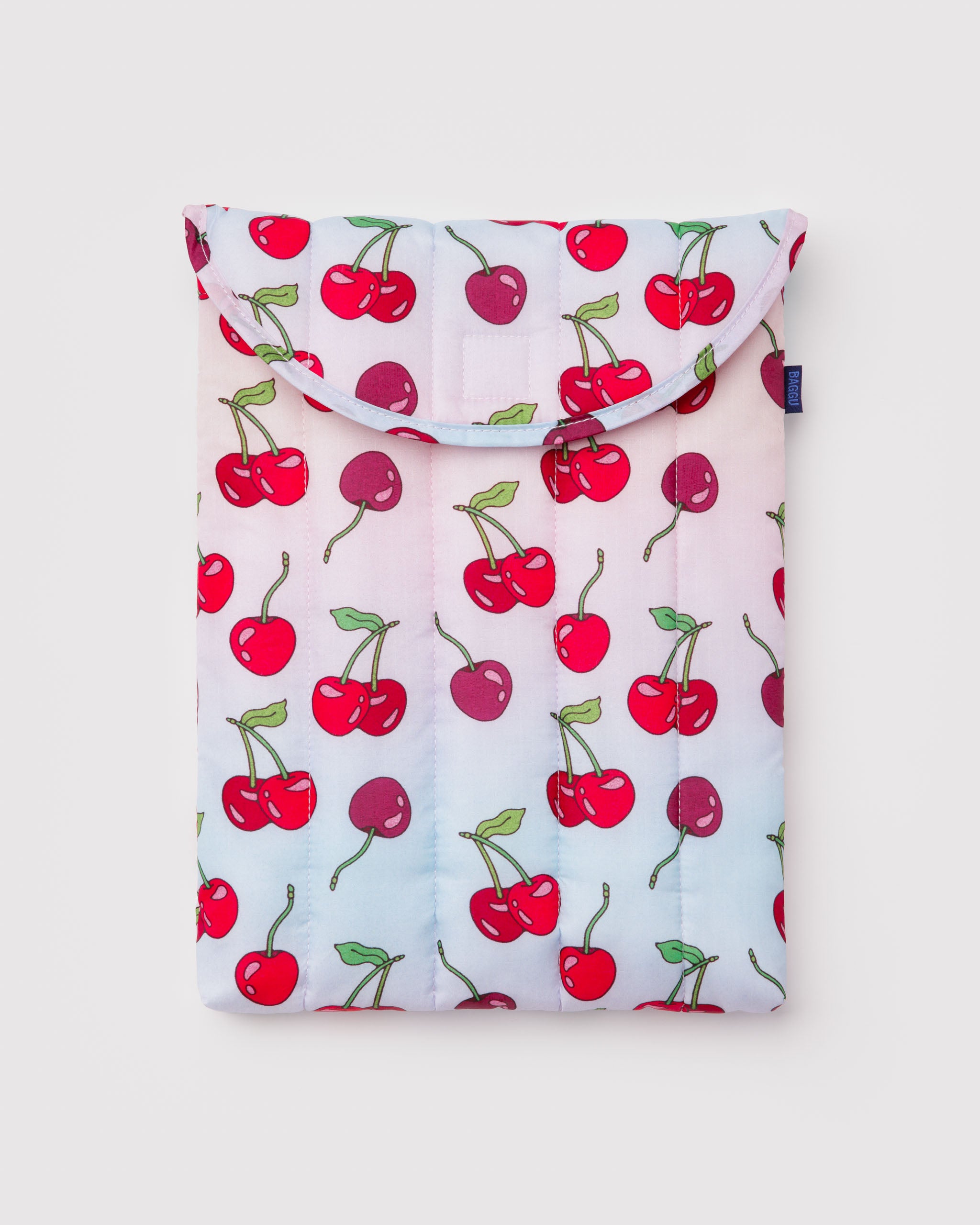 Pink and blue quilted and puffy laptop sleeve with cherries pattern and BAGGU logo tag at the side.