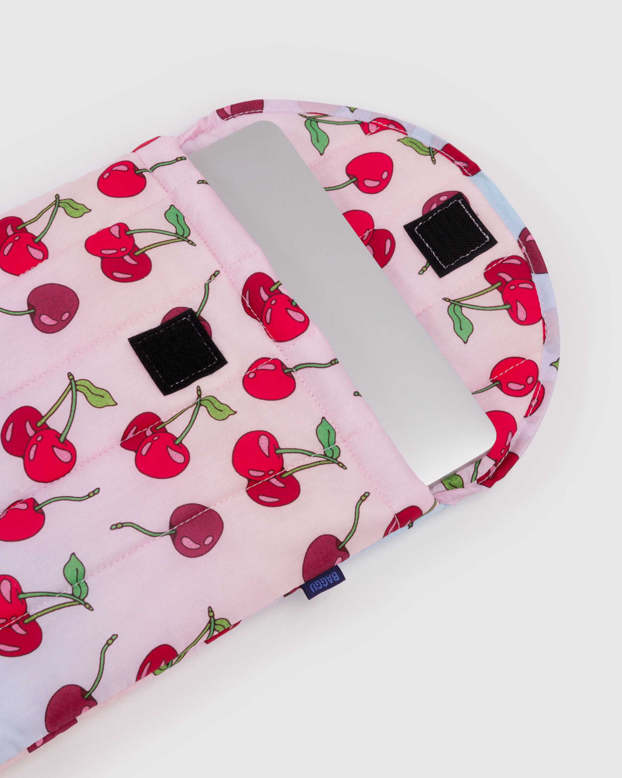 Pink quilted sleeve with red cherry pattern and velcro closure with silver laptop inside.