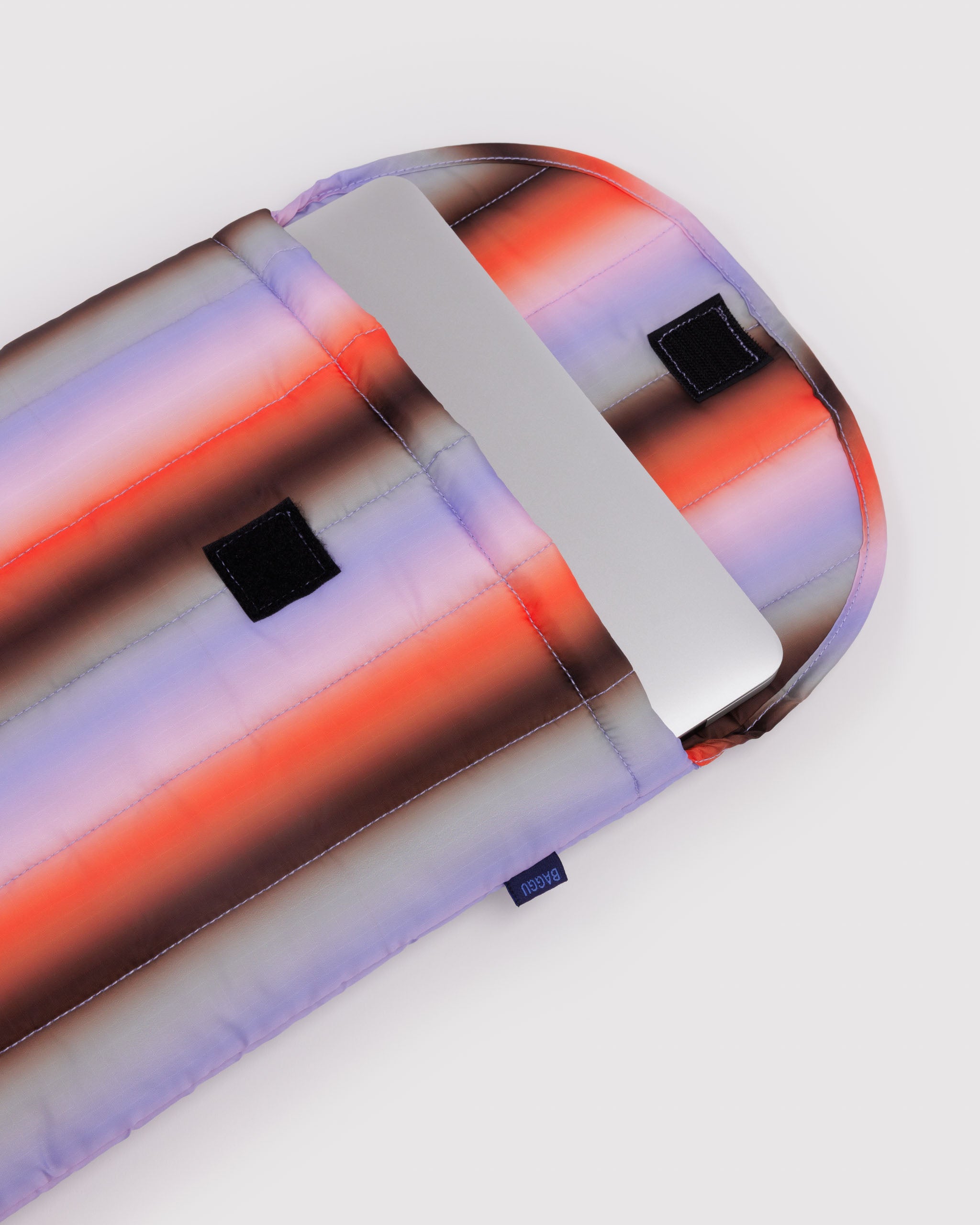 Open puffy and quilted sleeve with gradient coloured stripes and a silver laptop inside and velcro closure.