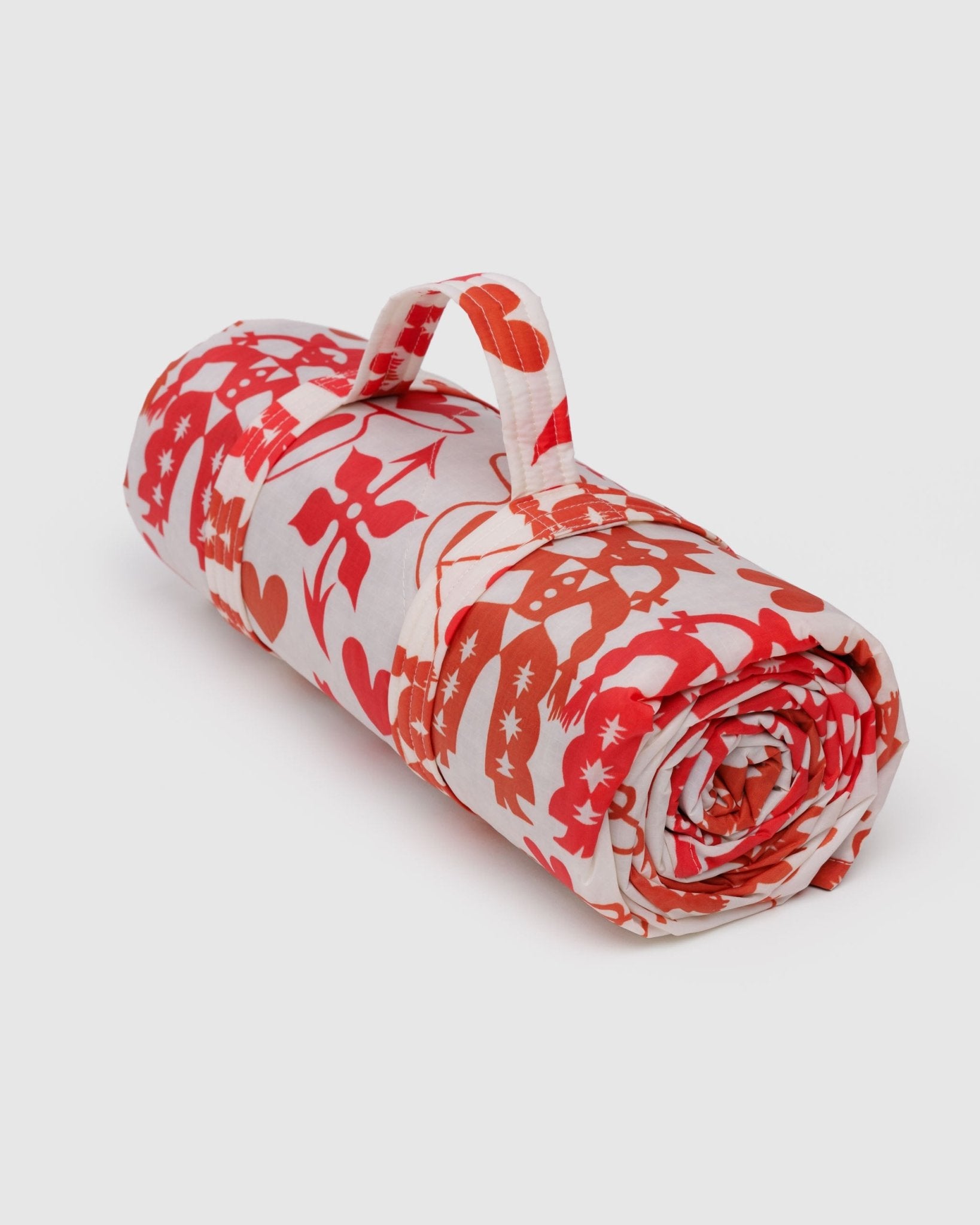 Rolled-up quilted picnic blanket with red cowgirl and heart patterns and a carry handle.