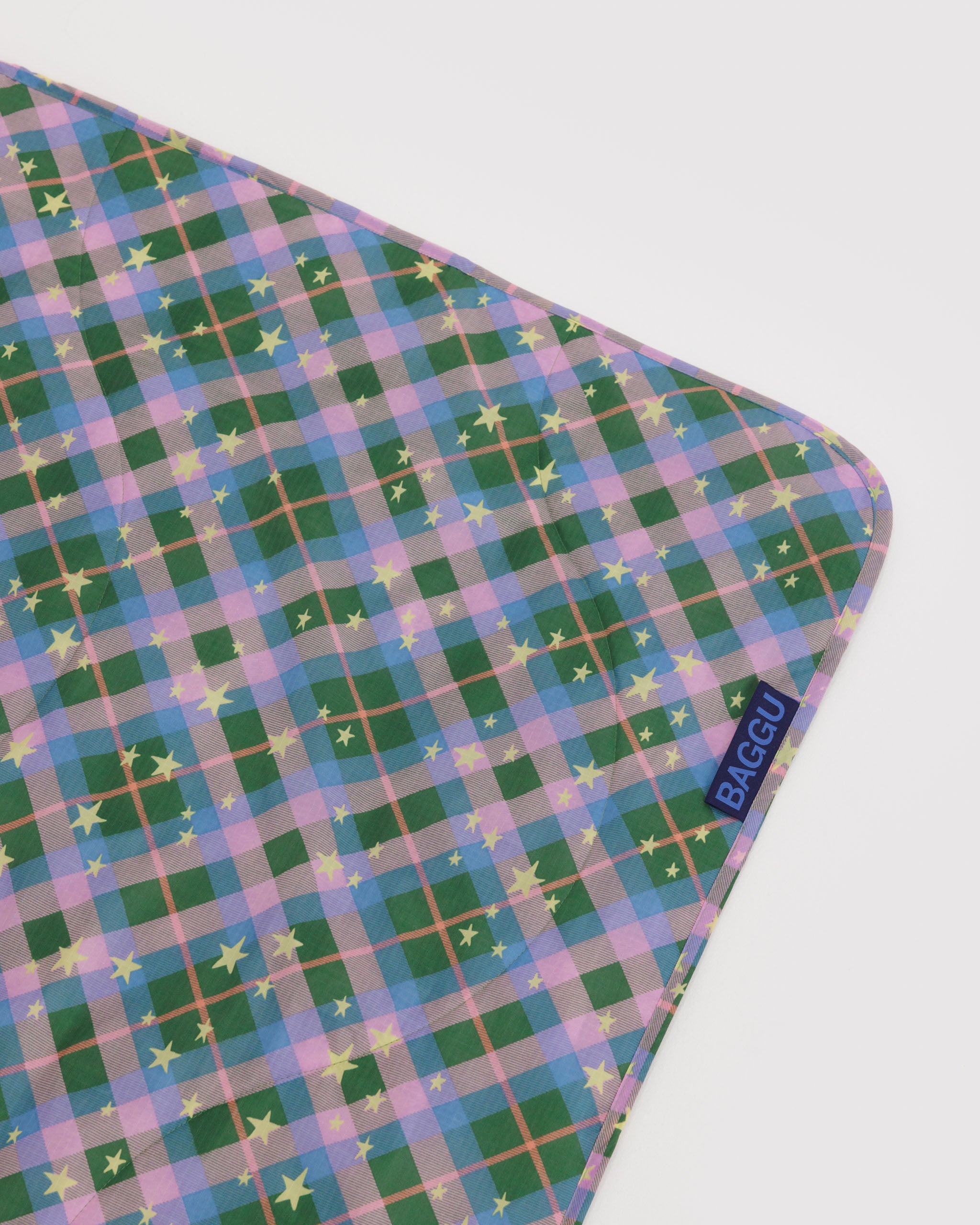 Green plaid patterned blanket with gold stars and 'BAGGU' logo at edge