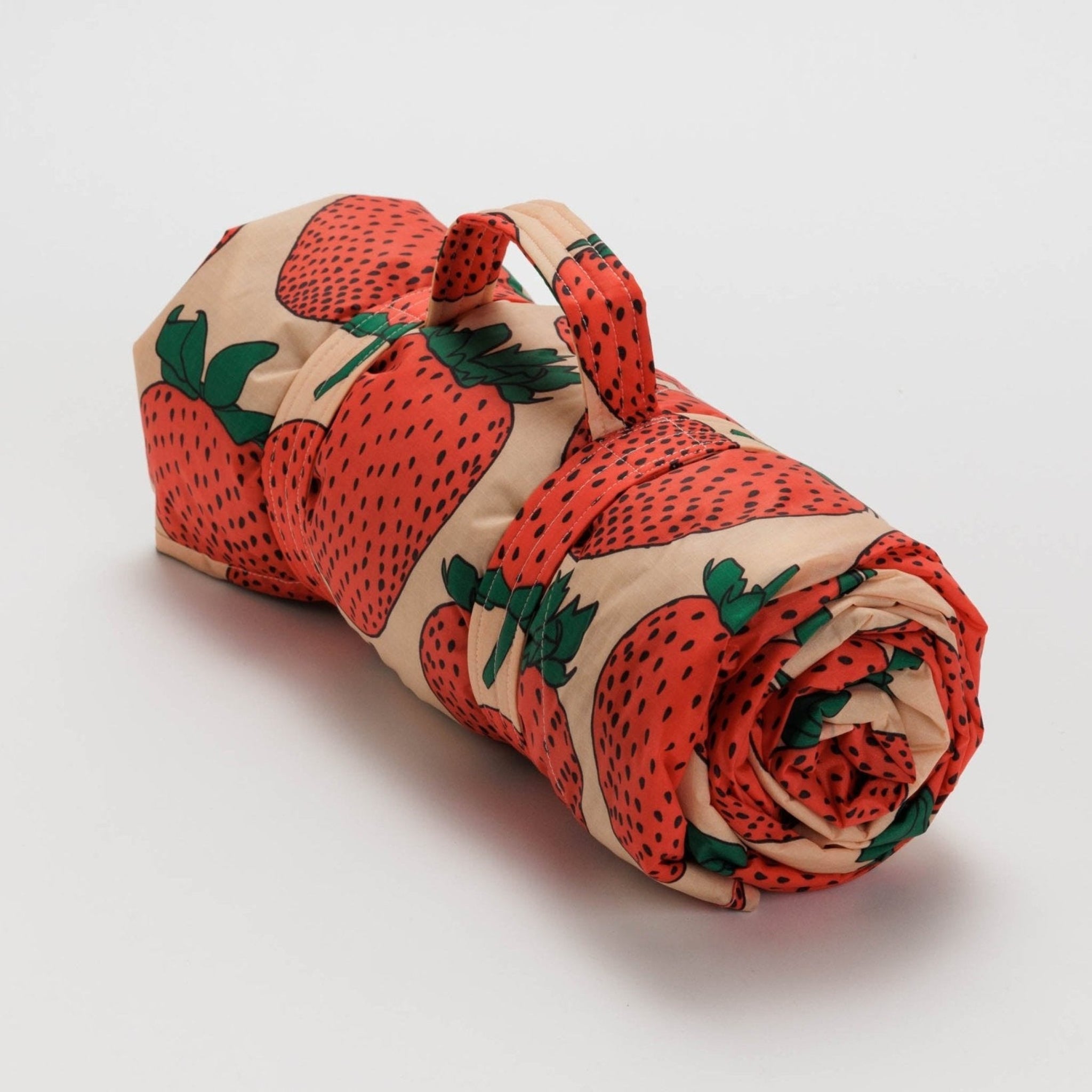Rolled up Baggu Puffy Picnic Blanket in Strawberry pattern with carry handle