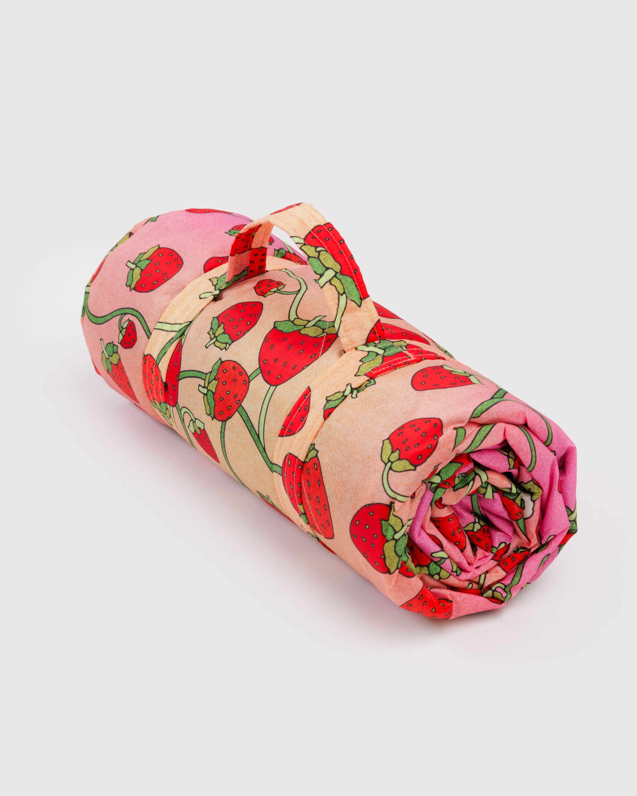 Rolled-up quilted and puffy rug with strawberry pattern and a carry handle.