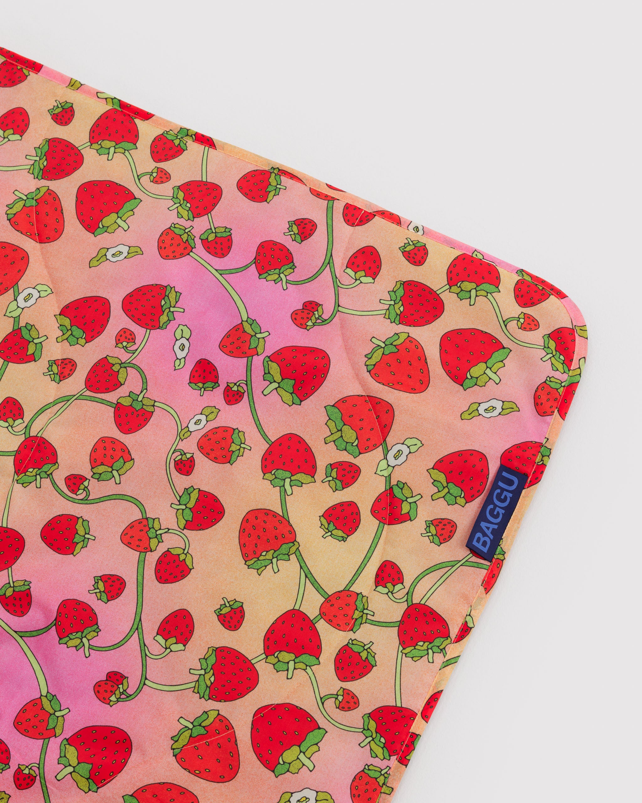 Pink with red strawberry pattern on quilted and puffy picnic rug.