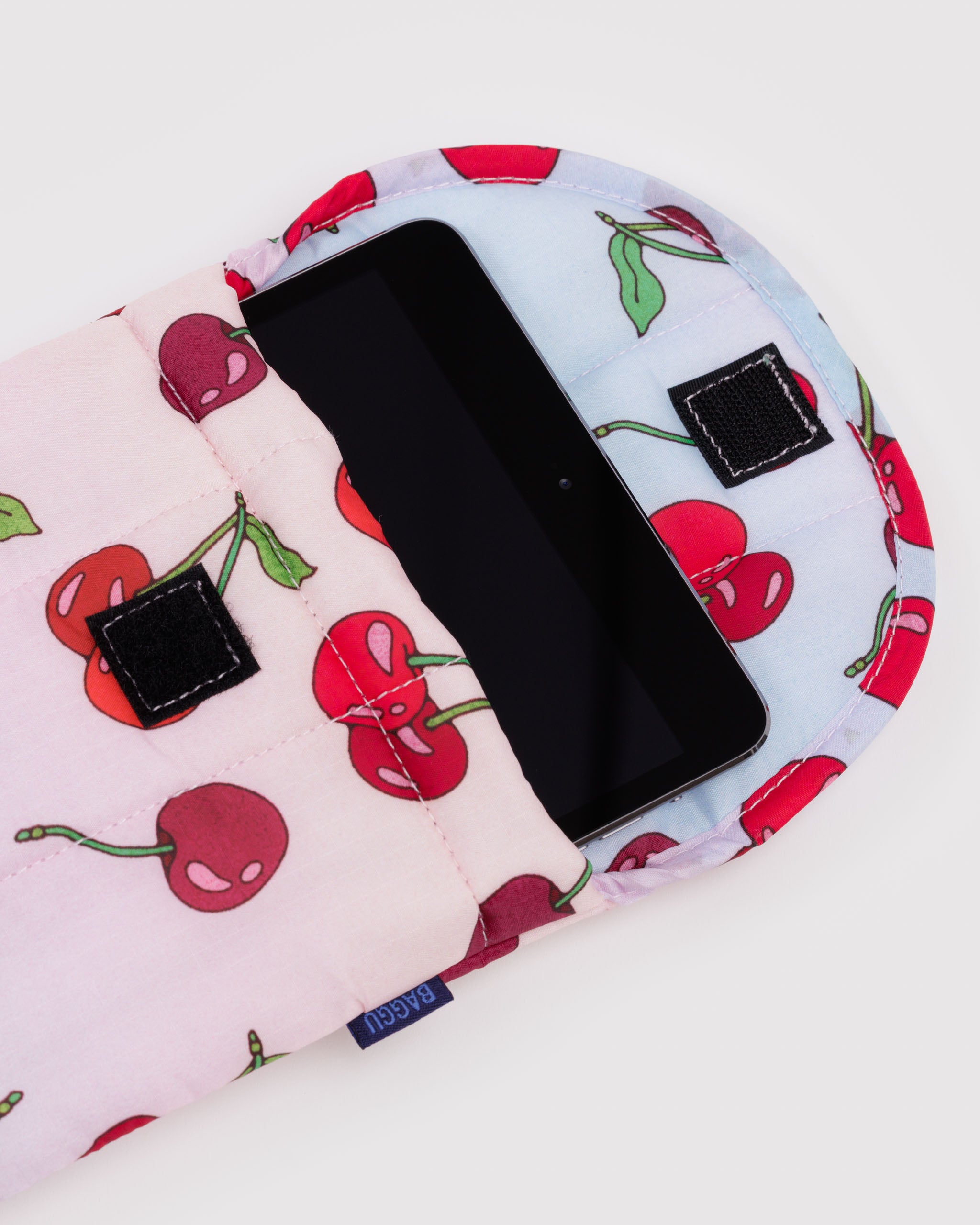 Puffy and quilted tablet sleeve with cherry pattern and velcro closure with a black iPad tablet inside.