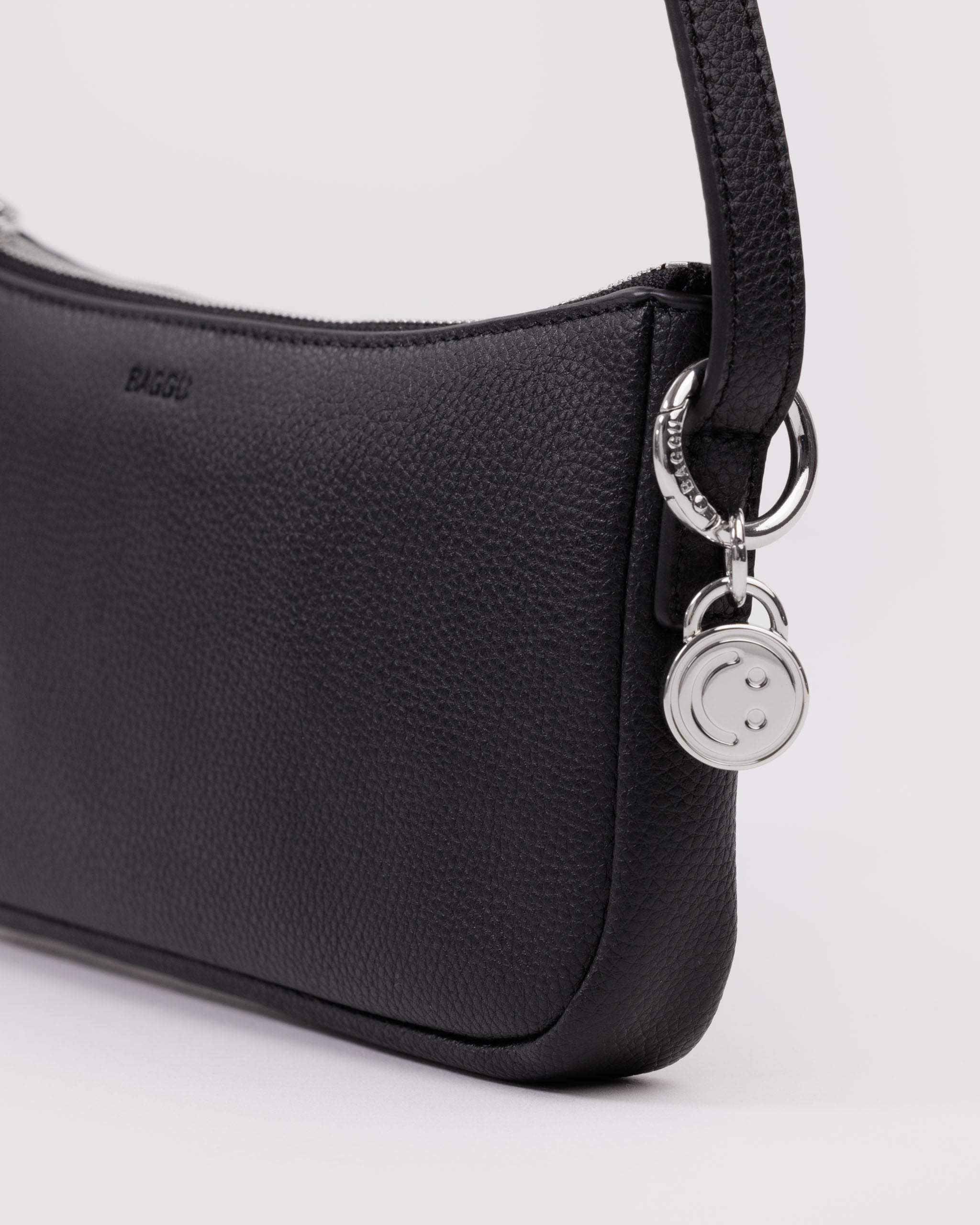 Black leather handbag with a silver metal smiley face bag charm attached to shoulder strap by a BAGGU branded metal silver ring.