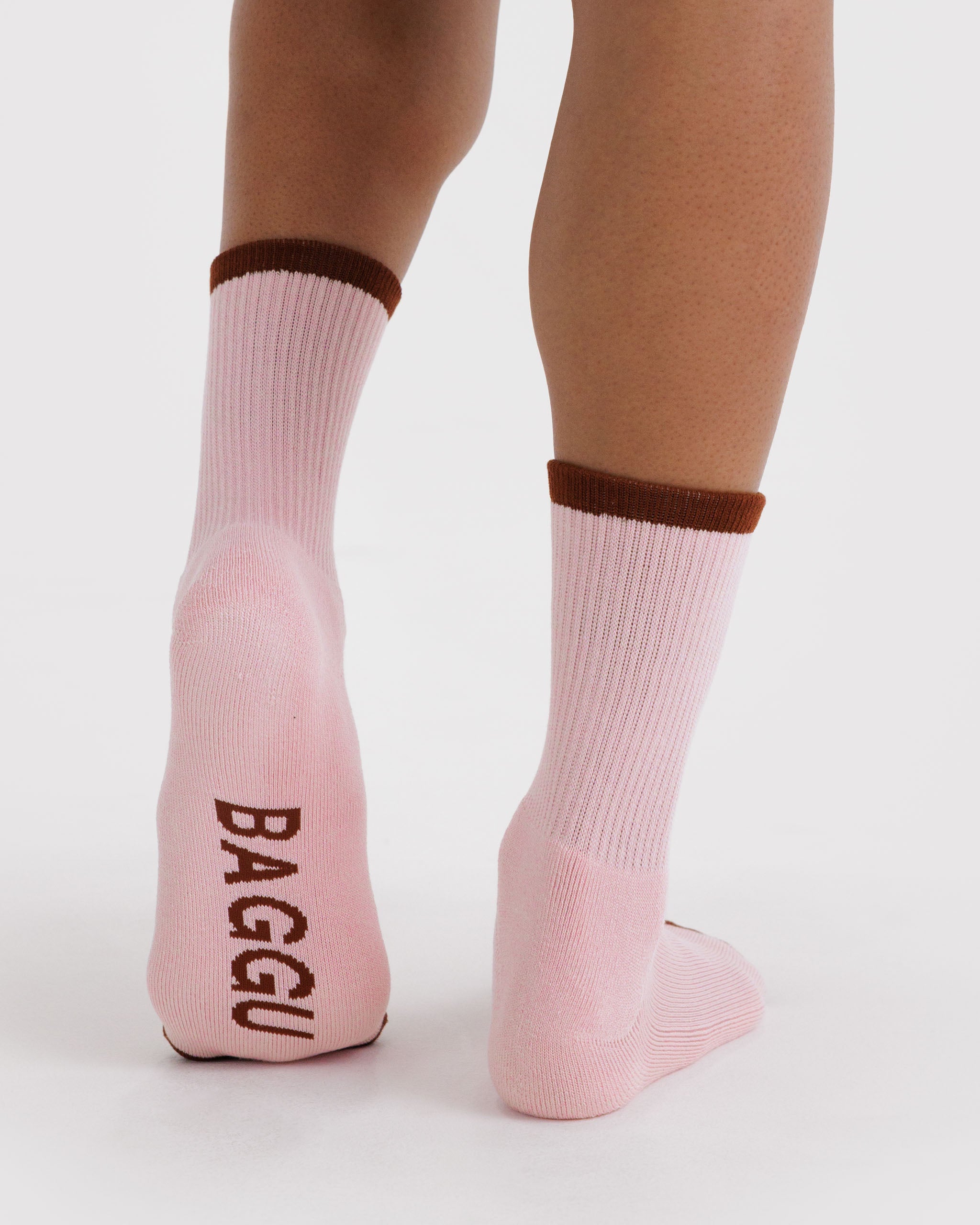 Pink ribbed socks with brown accents worn by a person with BAGGU logo on sole.