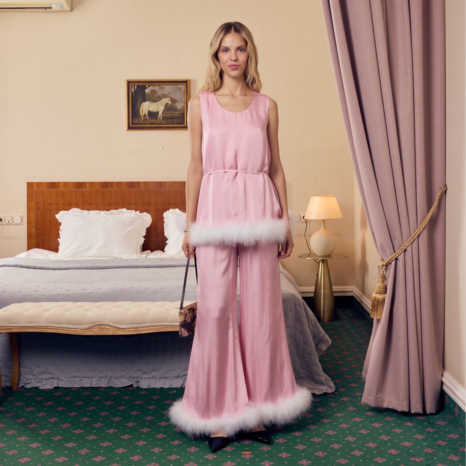 Woman in a pink top and pants with white feathers trim standing in a bedroom.