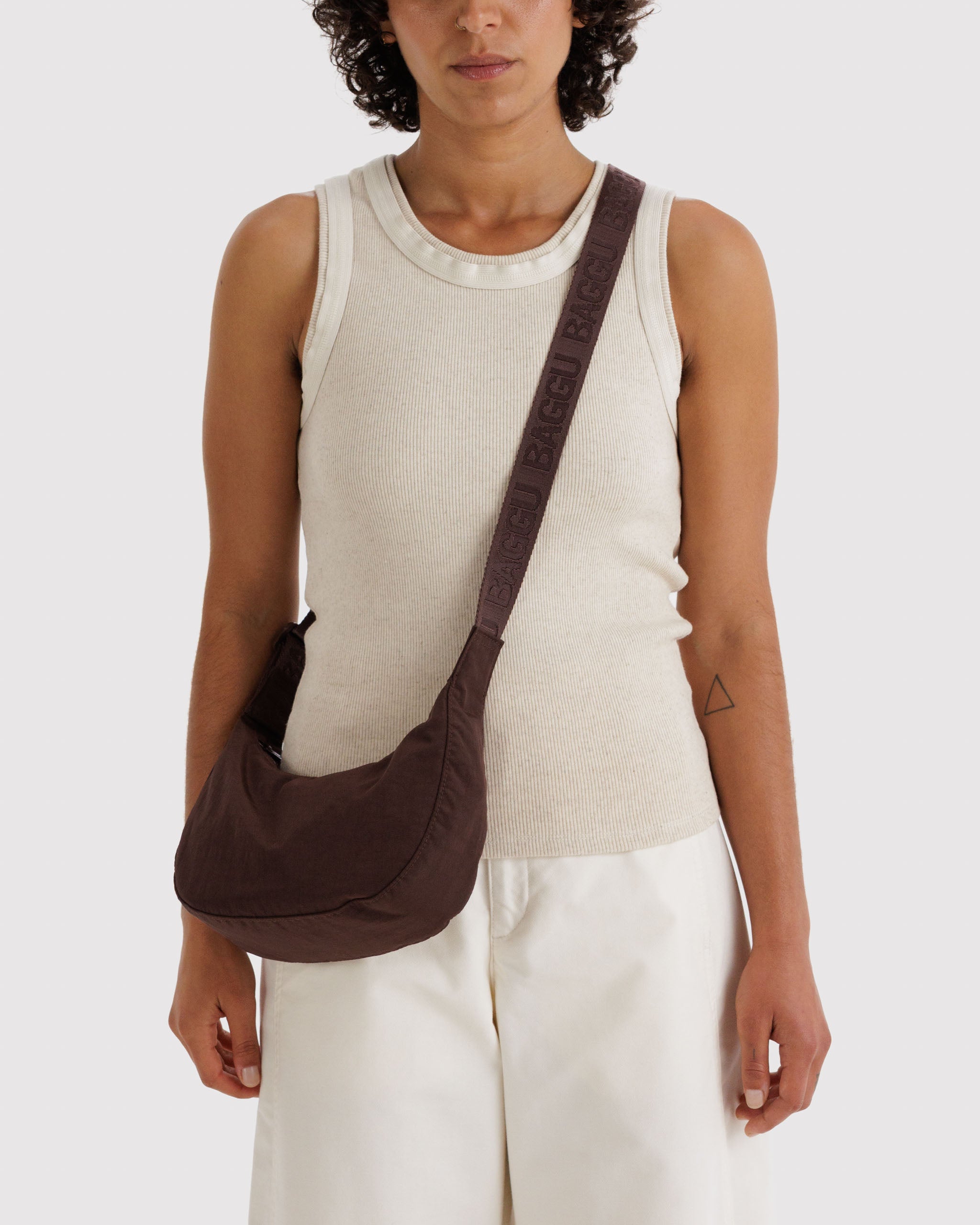 Woman wearing a brown shoulder bag crossbody style with a wide adjustable strap.