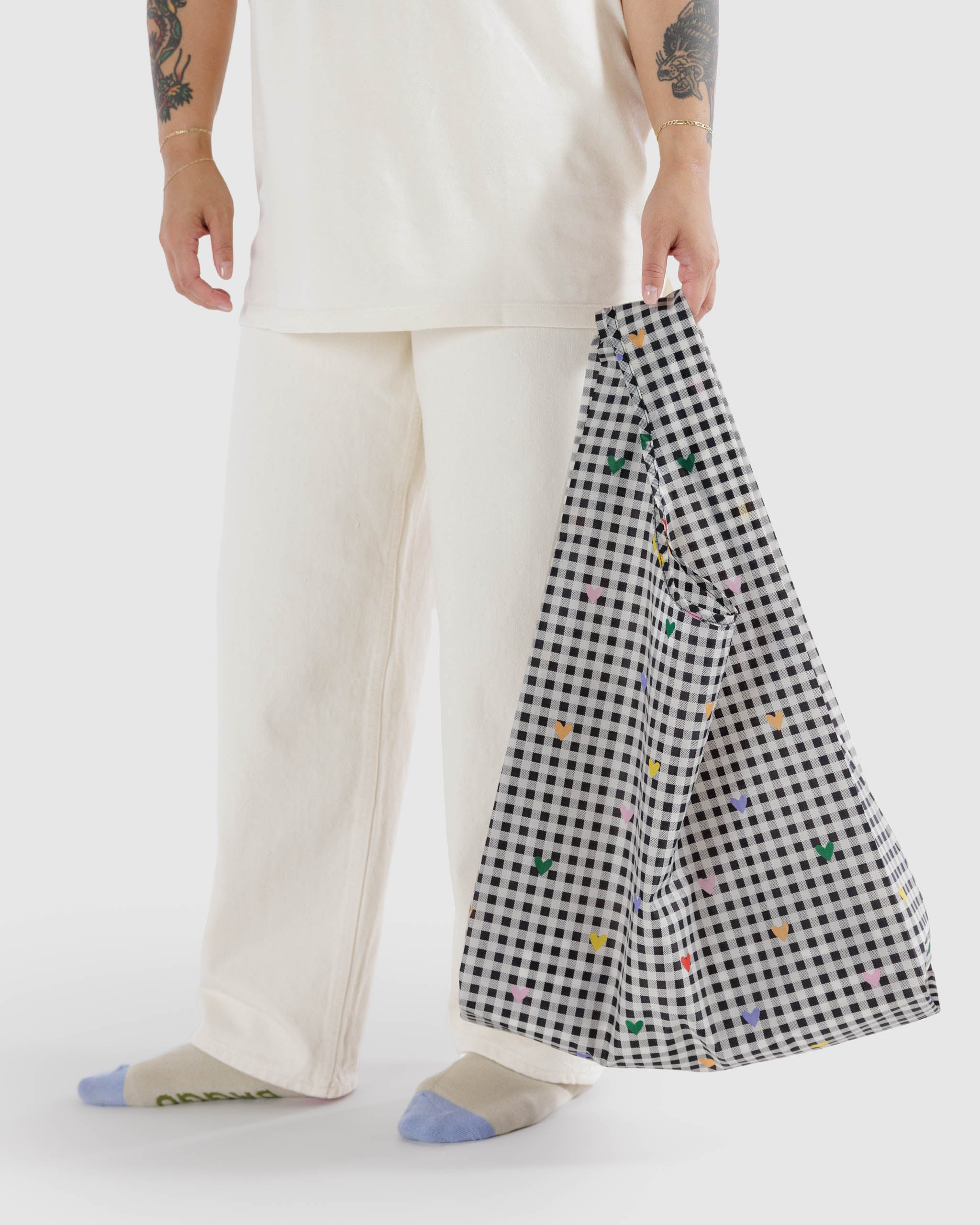 Woman-holding-in-hand-Baggu-standard-bag-in-black-gingham-with-pastel-coloured-hearts-print