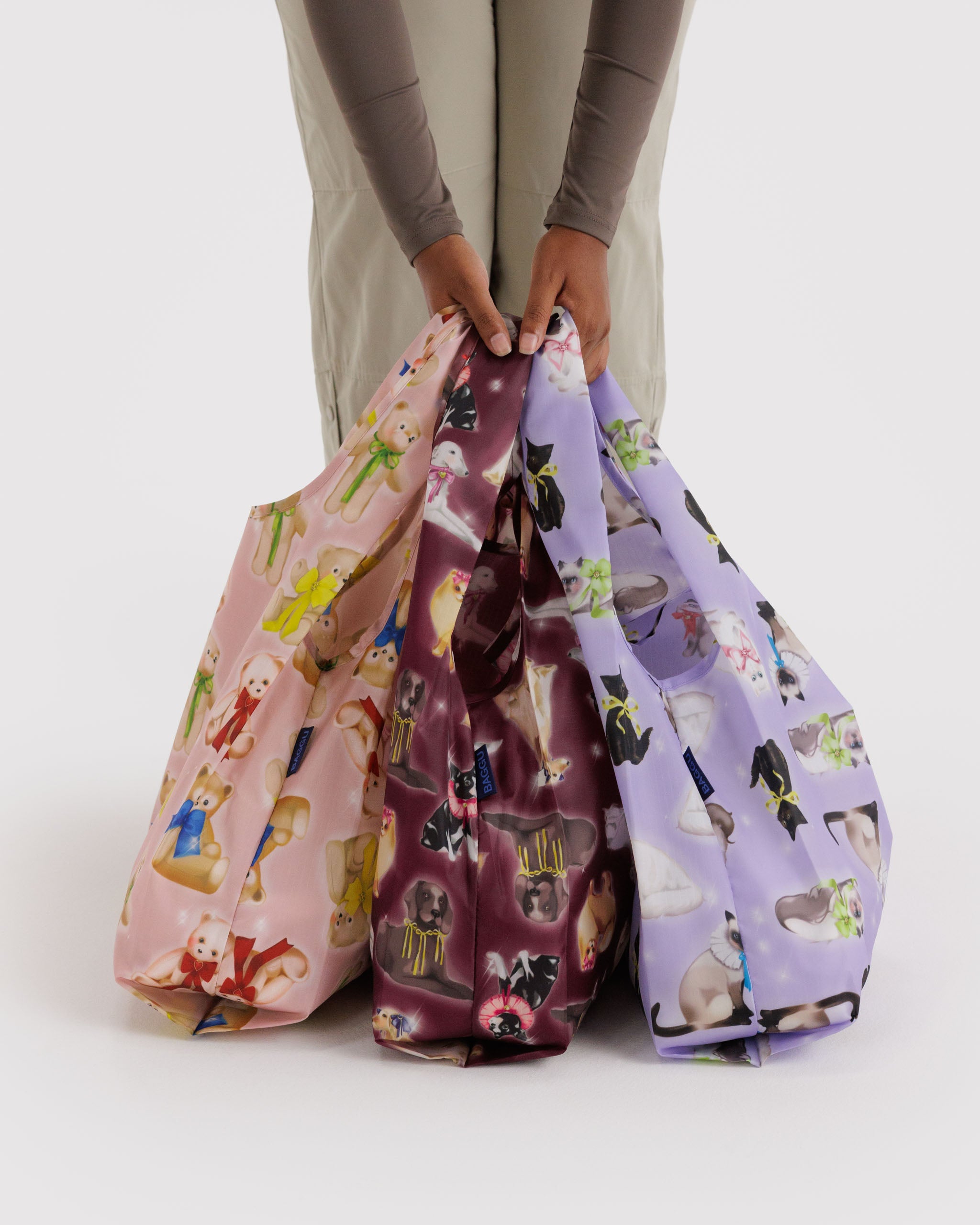 Three patterned bags held by a person in fancy cat, dog and teddy prints.