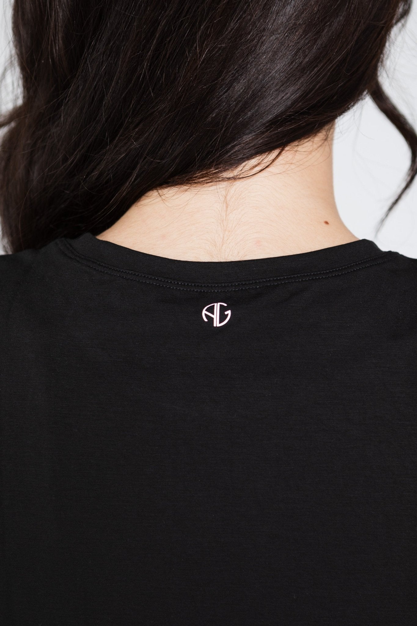 Close up of AG logo at back yoke of black tank being worn by a woman.