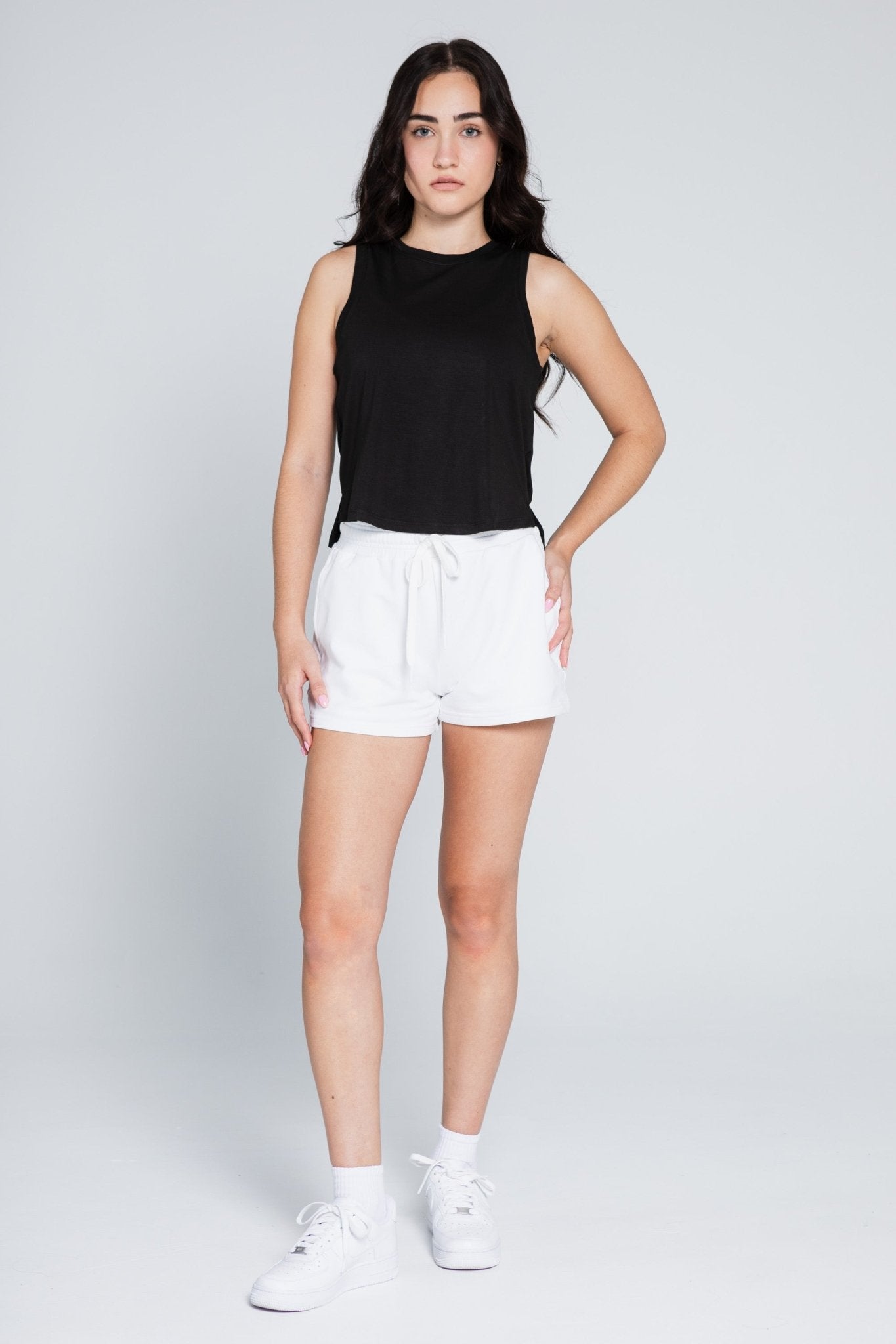 Woman wearing a black tank top with high low hem and white cotton shorts with drawstring.
