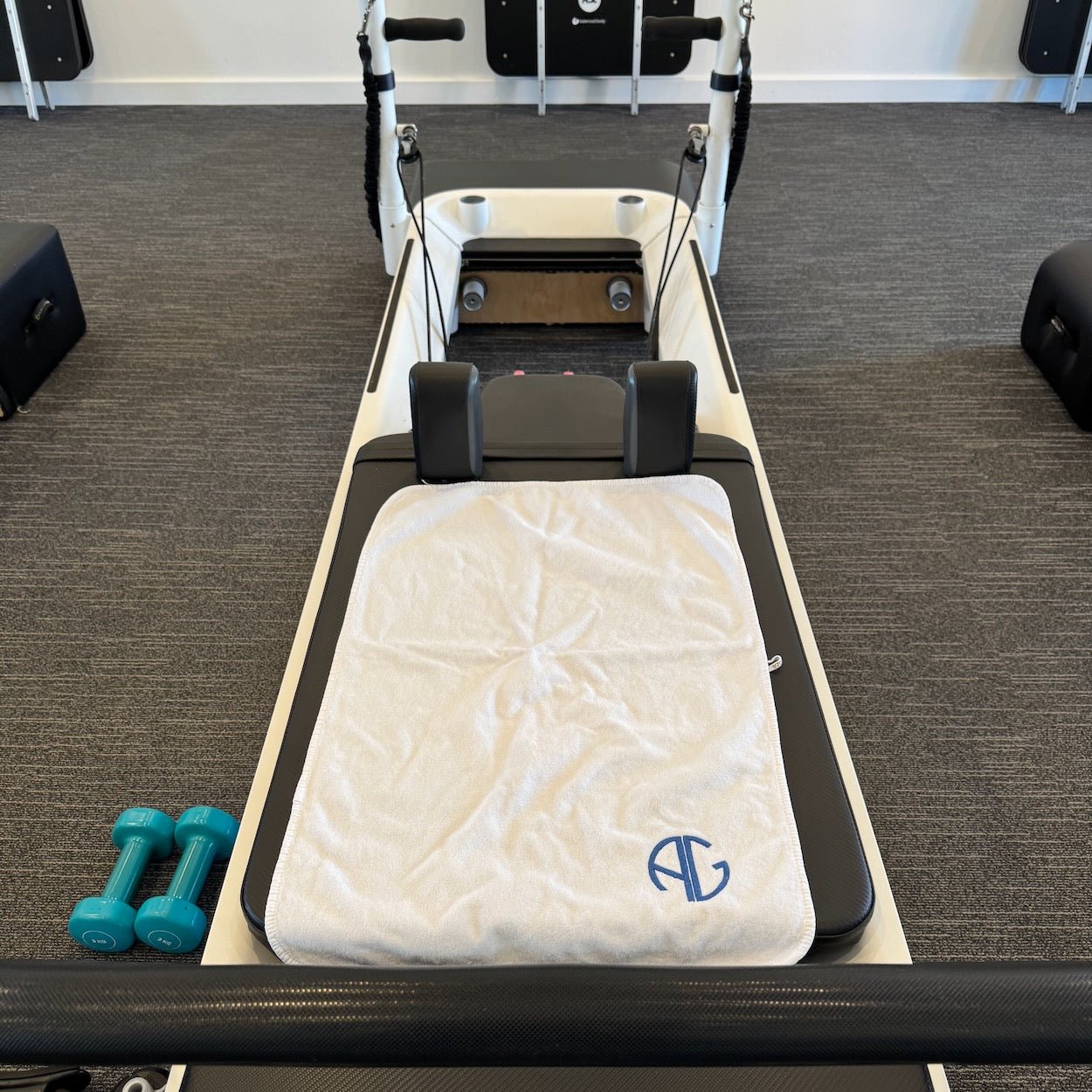 White sports towel with AG logo on pilates bench in studio.