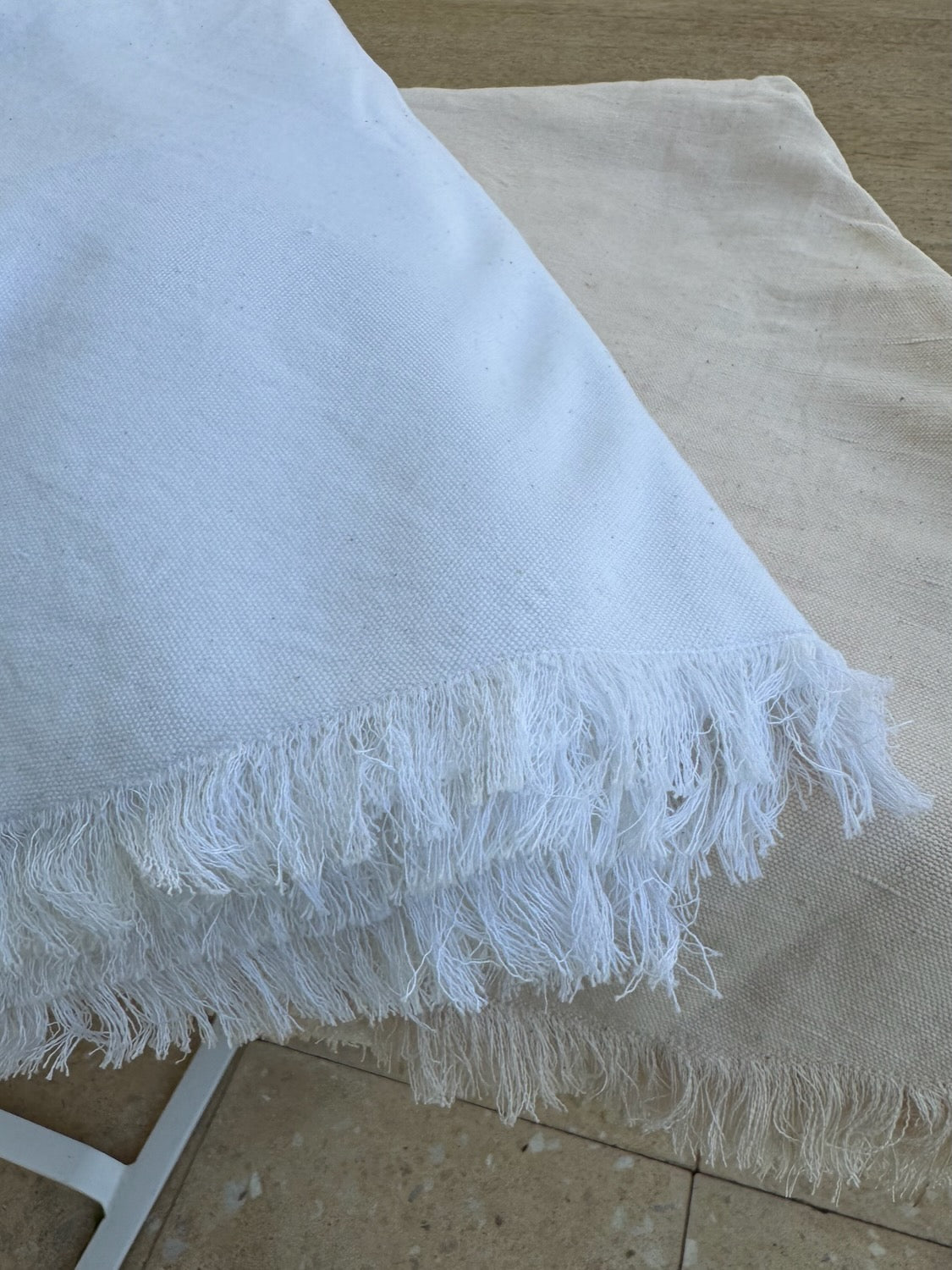 White and blush tablecloth with frayed edges folded and stacked on a table