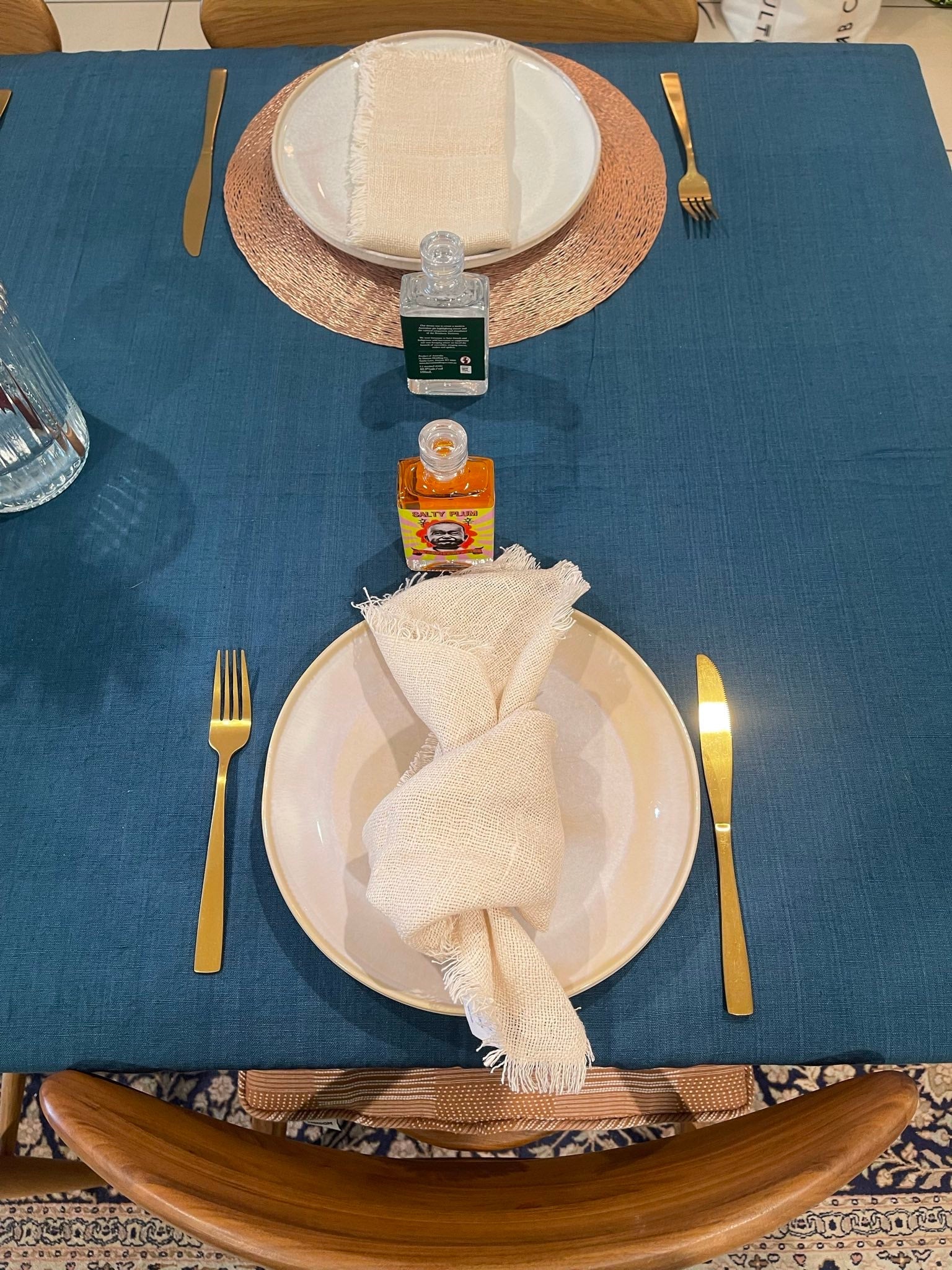 Teal tablecloth on a dining table set with plates, cutlery, and bottles.