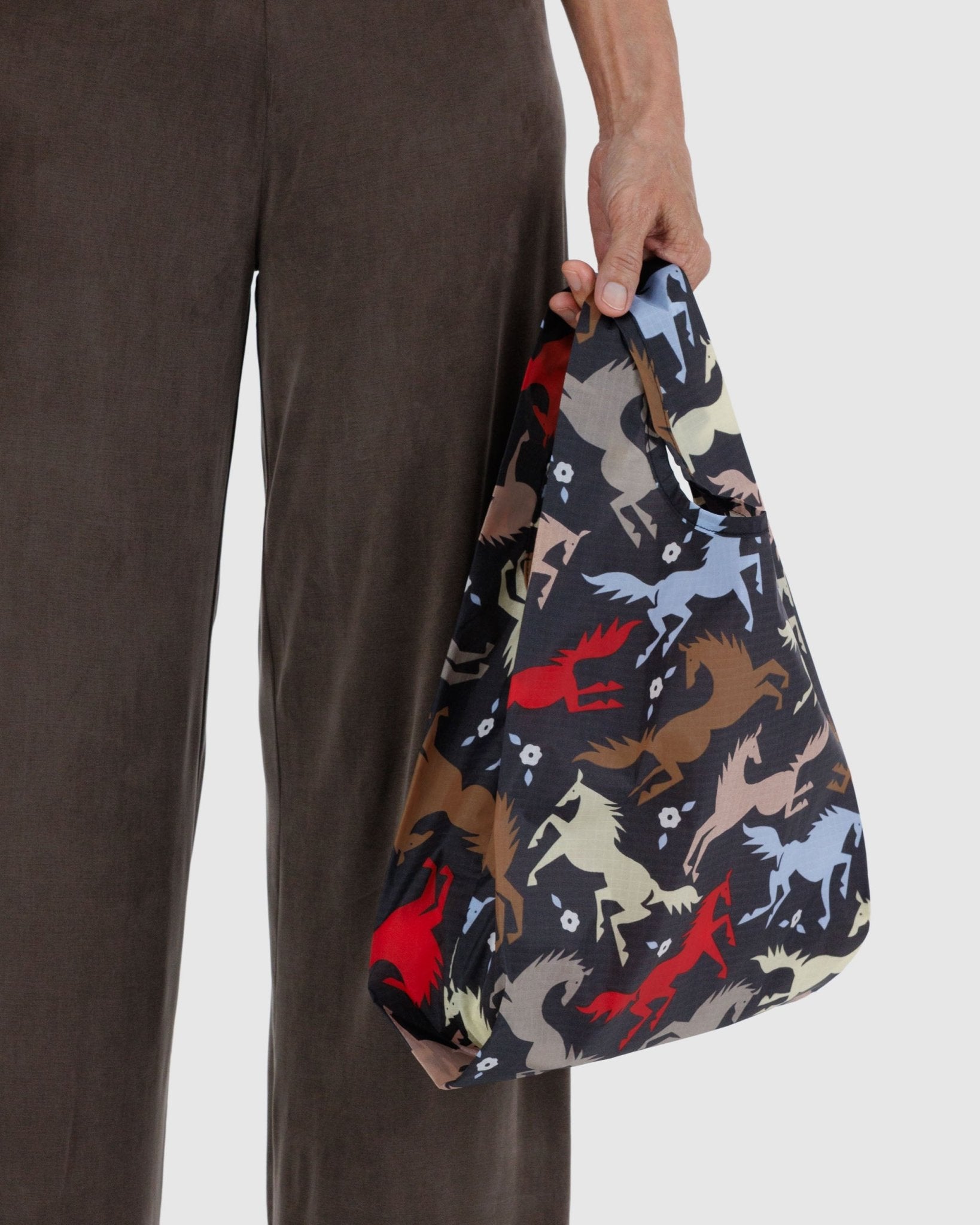Person holding a reusable bag with coloured horses and white flowers  pattern
