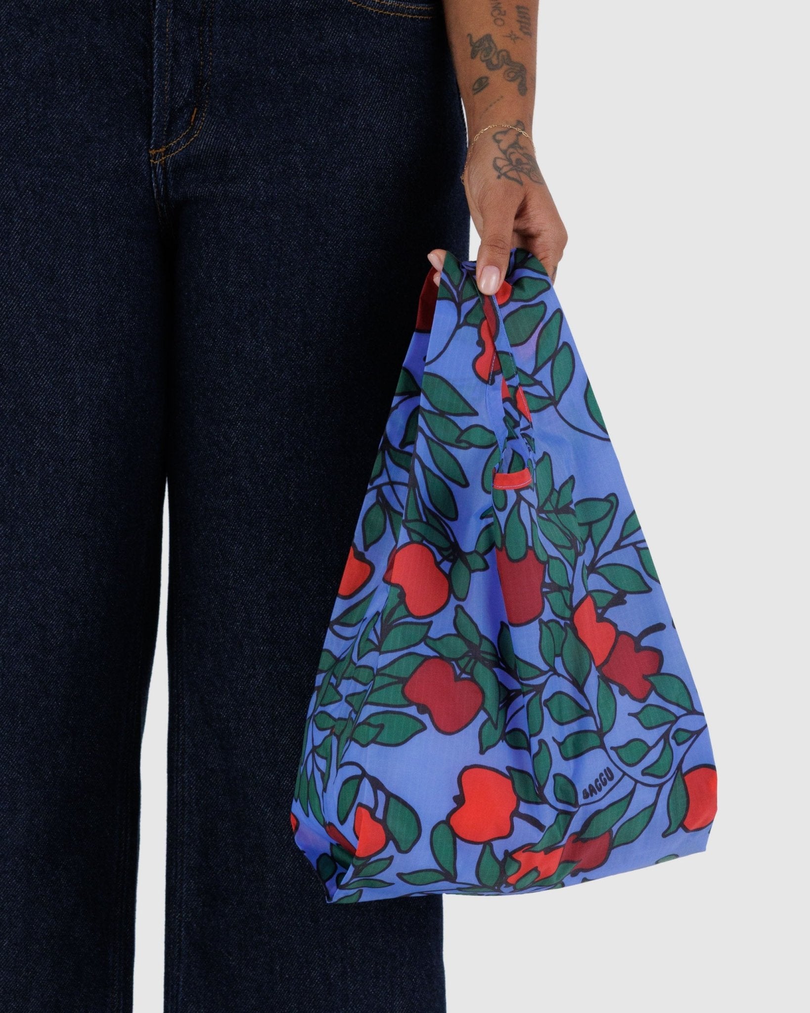 Person holding a small blue nylon reusable tote bag with red apples print in hand.