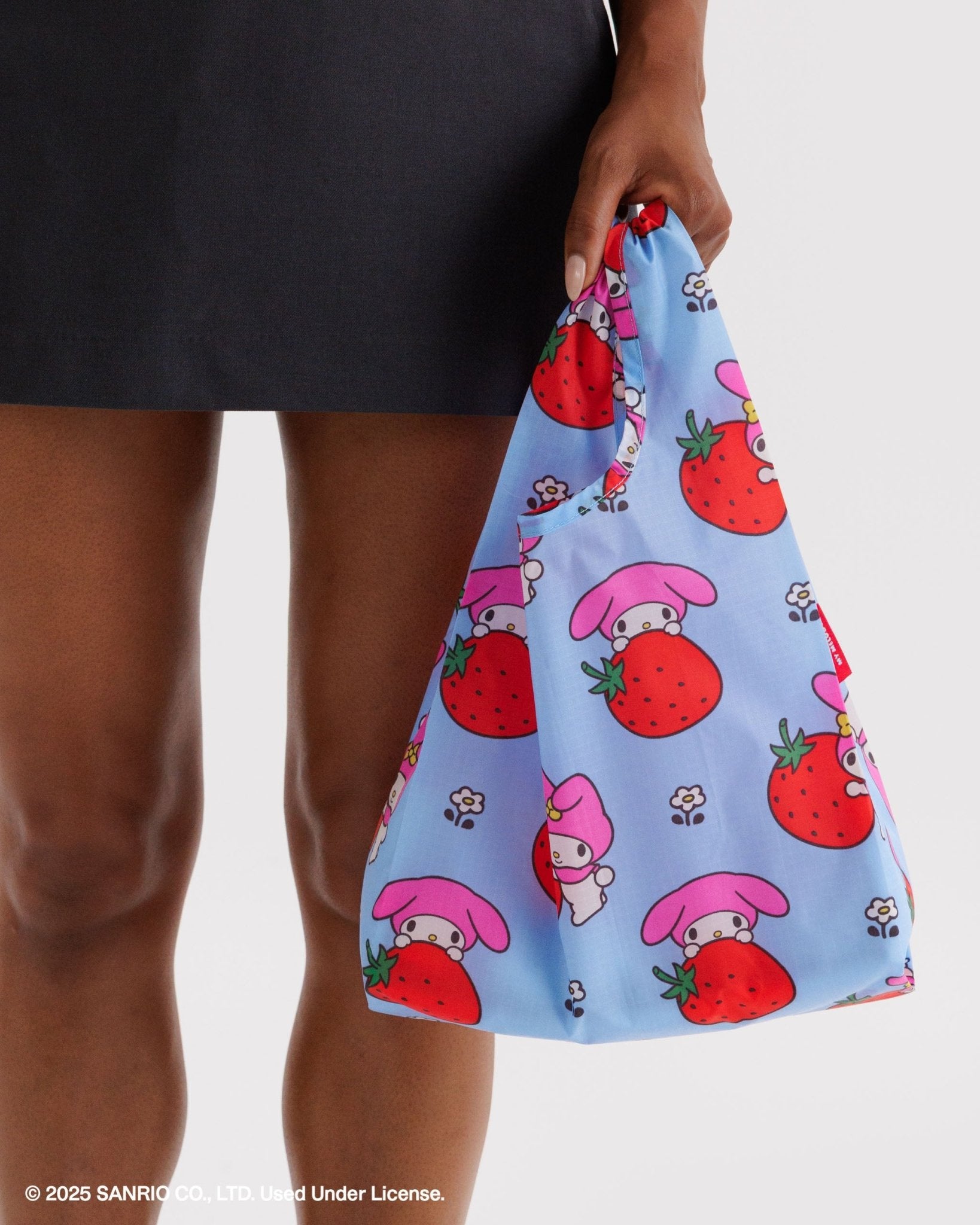 Blue baby size reusable bag with hello kitty character and strawberry pattern held by a person wearing a black skirt.