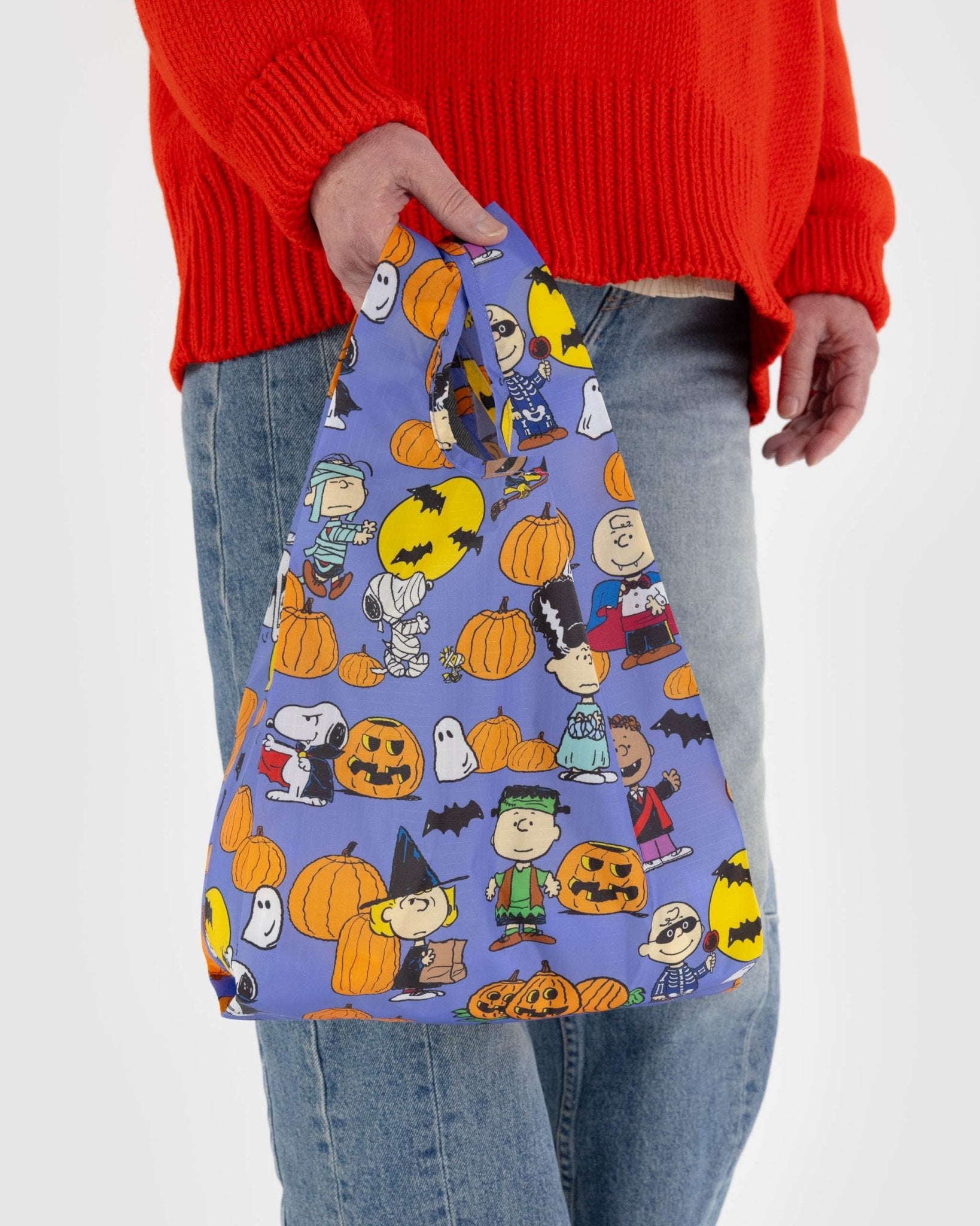 Person holding a baby sized reusable bag with peanuts characters and halloween pumpkins on blue for trick or treat