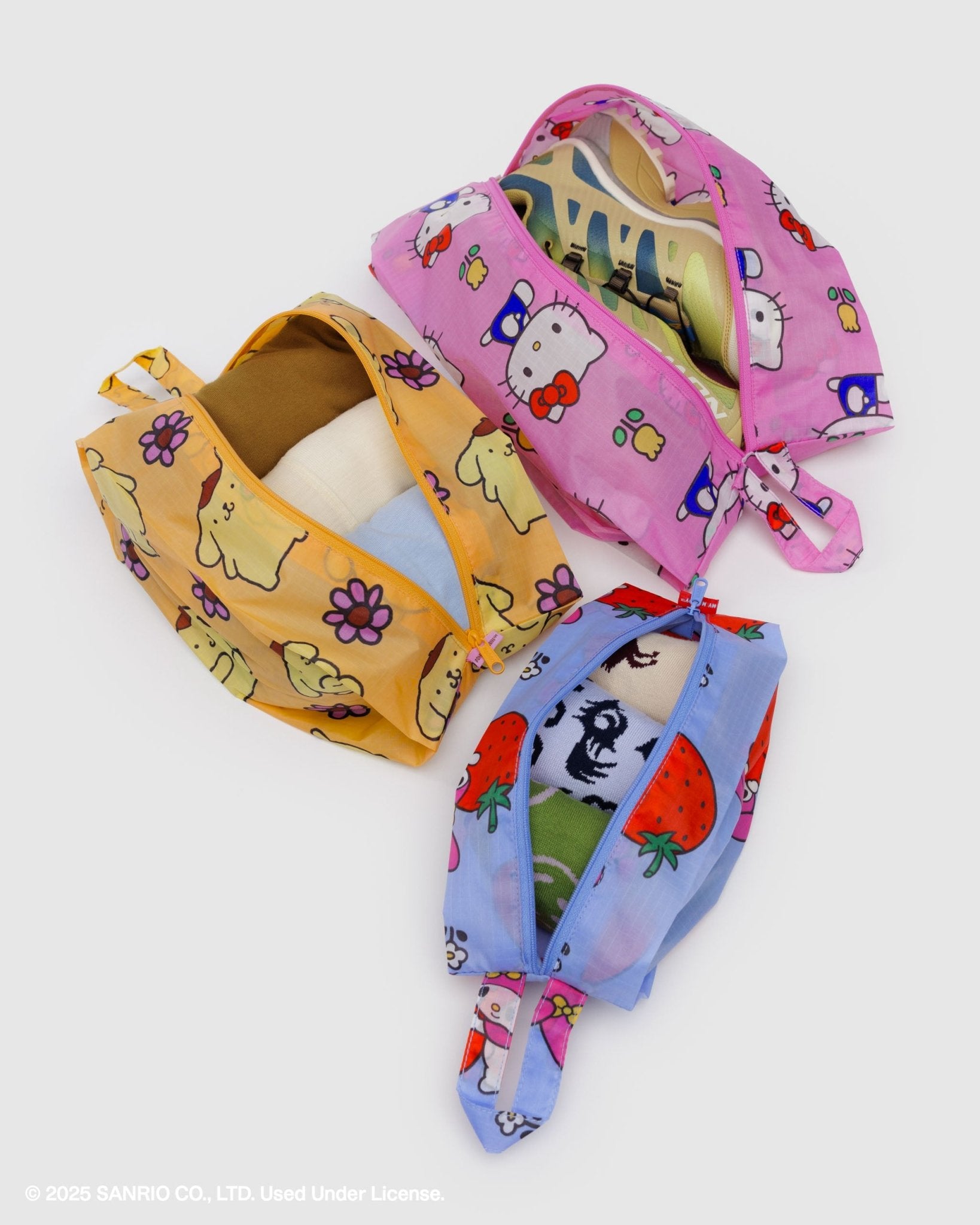 Three colourful zip top bags with hello kitty cartoon designs and zips open with shoes and clothing items inside and hanging loop