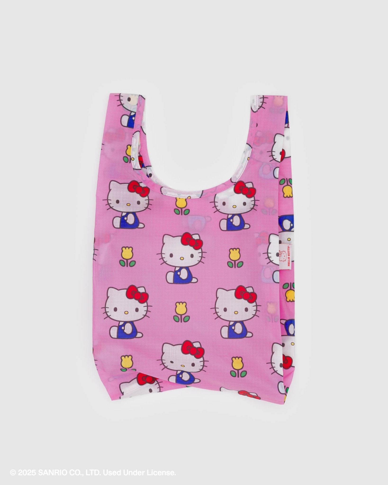 Pink reusable bag with print of a white cat wearing blue overalls with red bow near ear and yellow tulips
