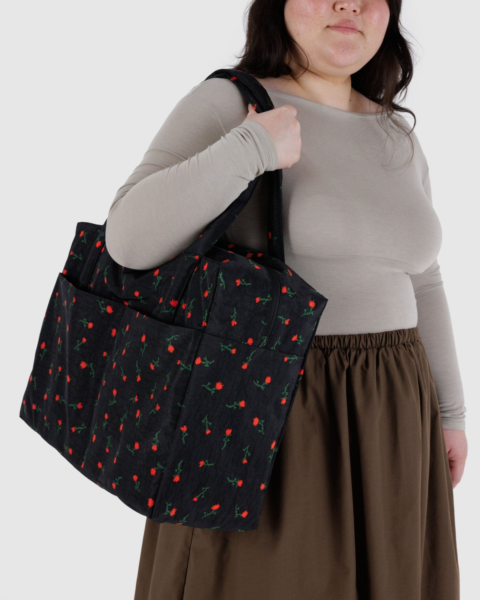 Person holding a black duffel bag with red wildflower pattern over shoulde