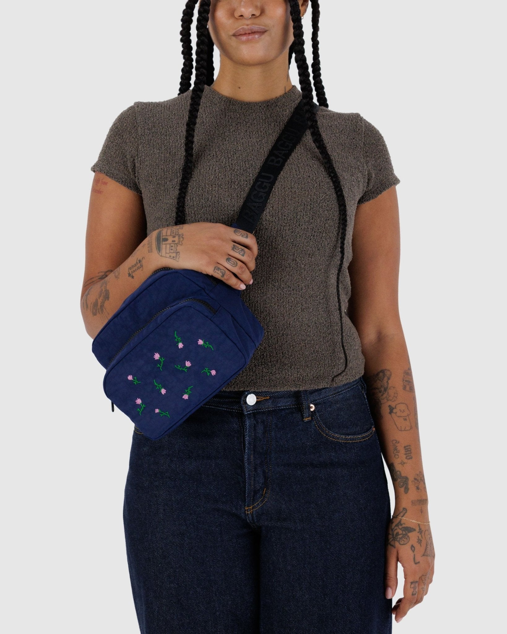 Person in jeans and top wearing a crossbody navy fanny pack bag featuring purple wildflower embroidery