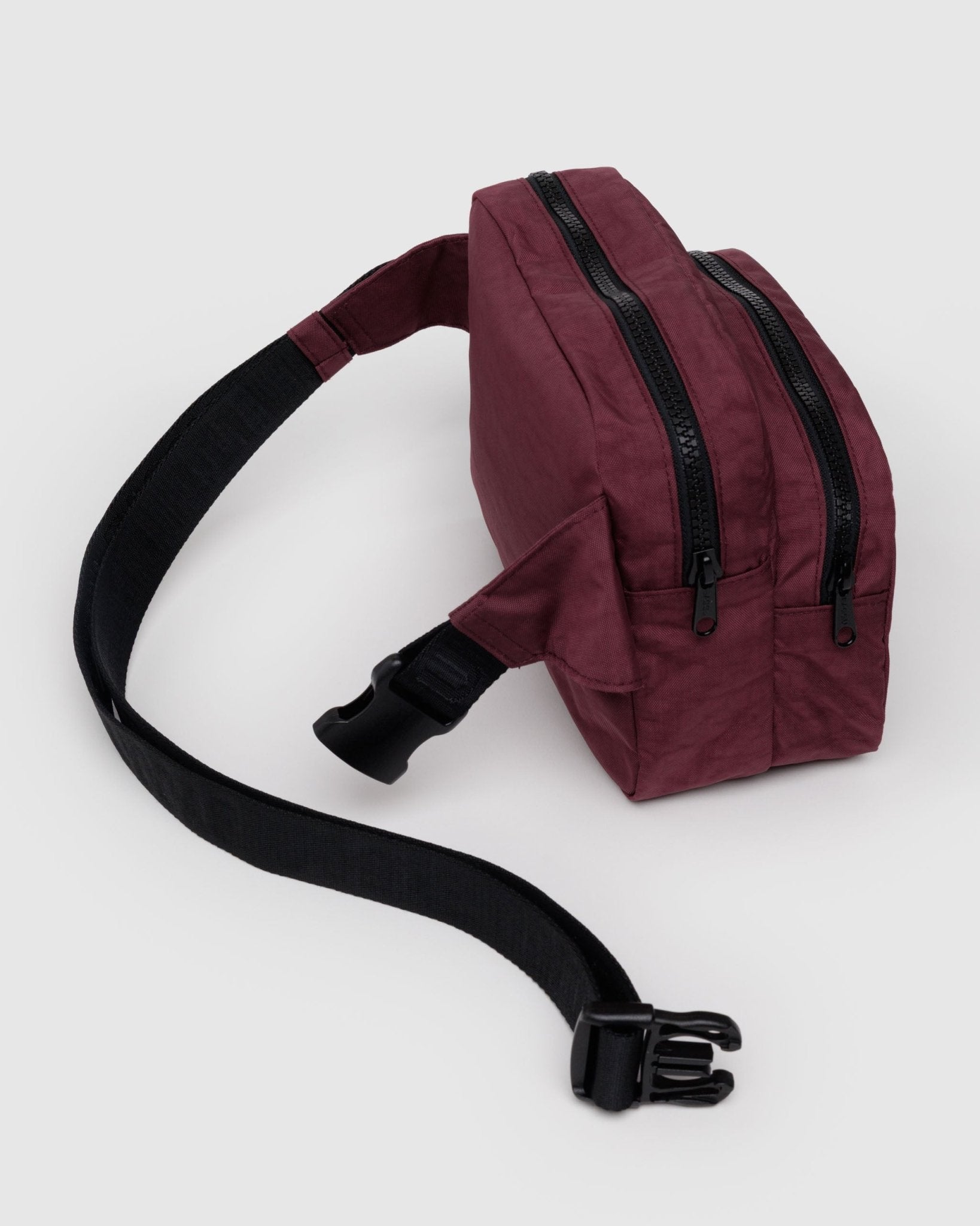 Maroon fanny pack with black zippers on two pockets and black adjustable strap with clip undone