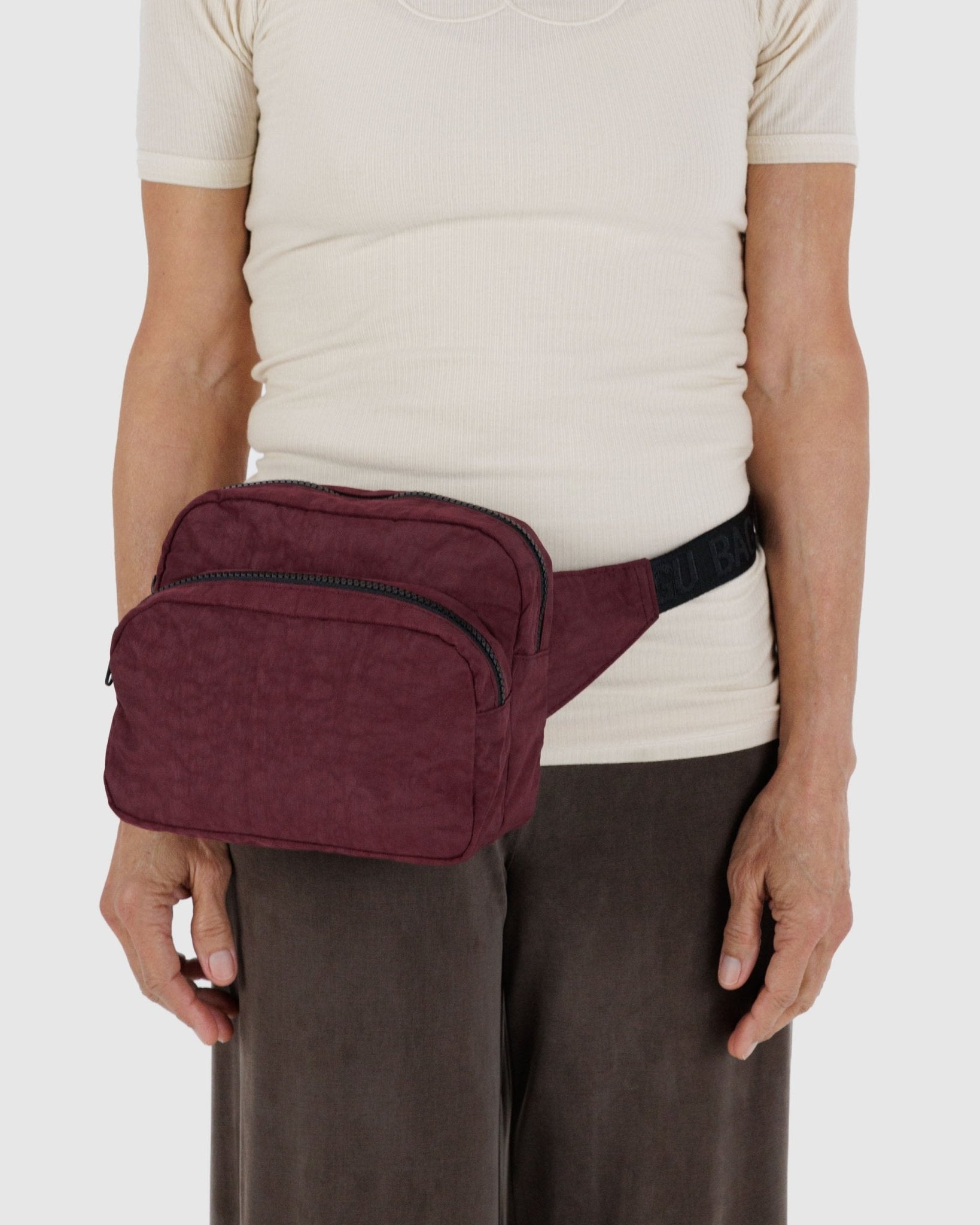 Person wearing a maroon waist bag with two zip pockets