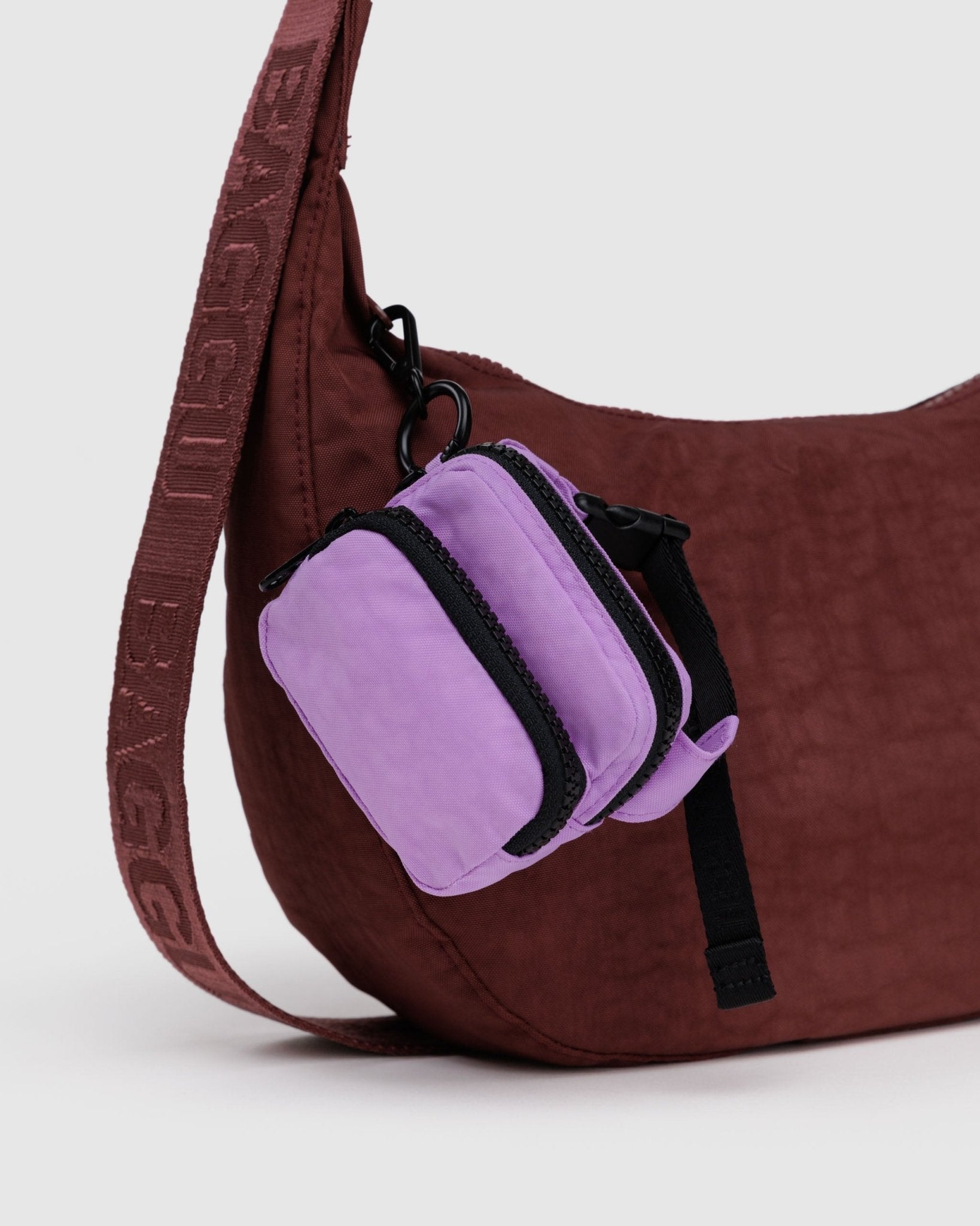 Burgundy shoulder bag with a purple fanny pack charm attached to zip